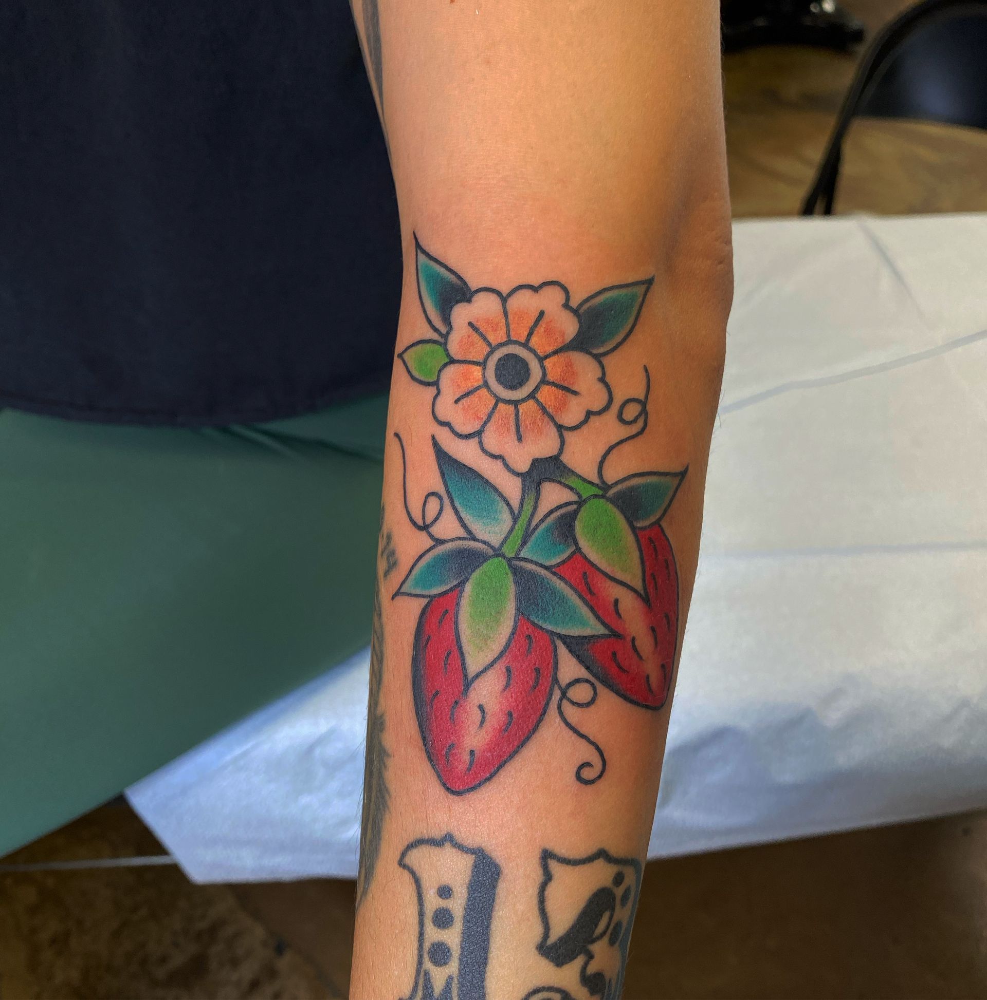 Arm tattoo: strawberries and flower with green leaves, red fruit, and orange center.