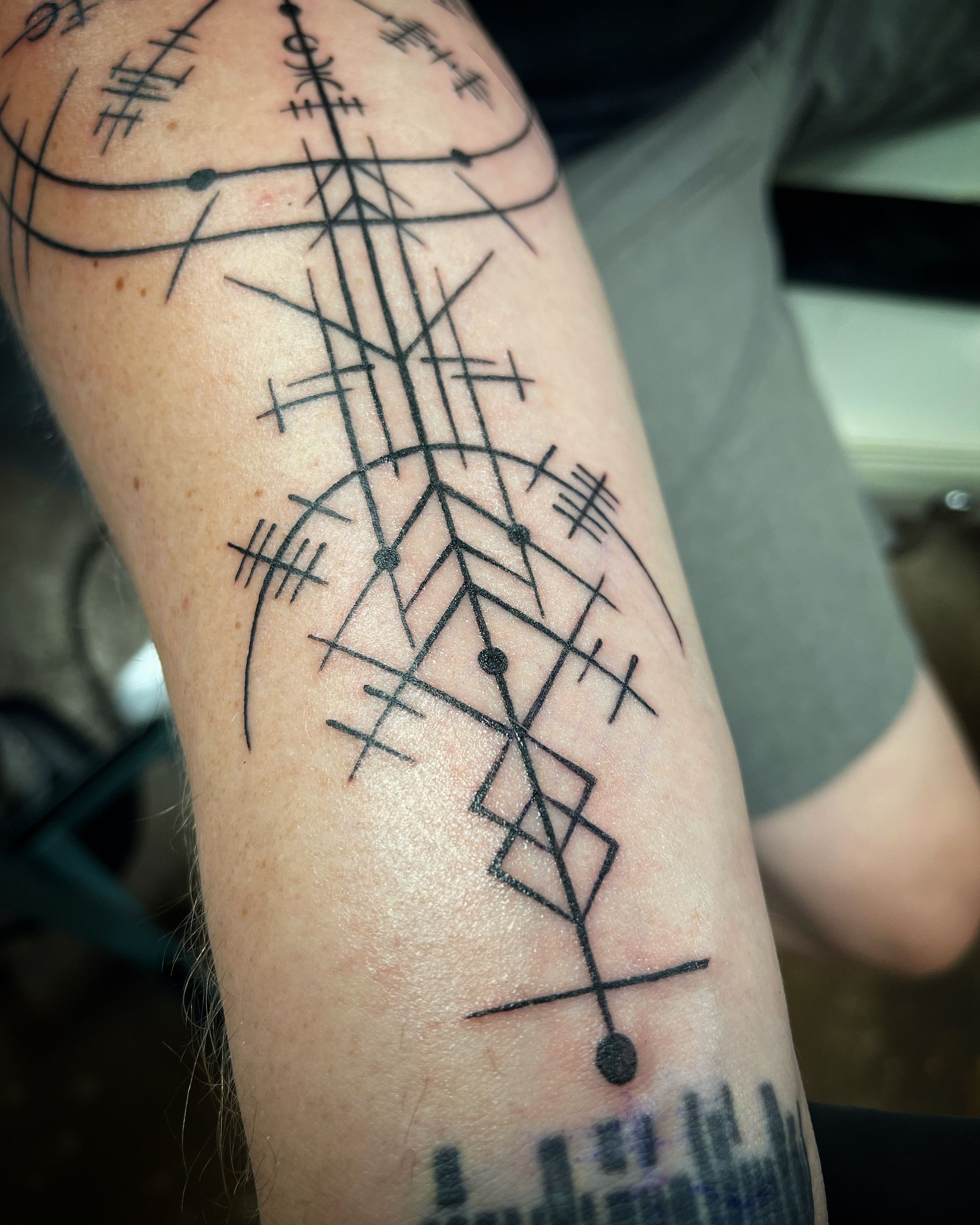 Geometric tattoo of lines, dots, and intersecting shapes on a forearm.