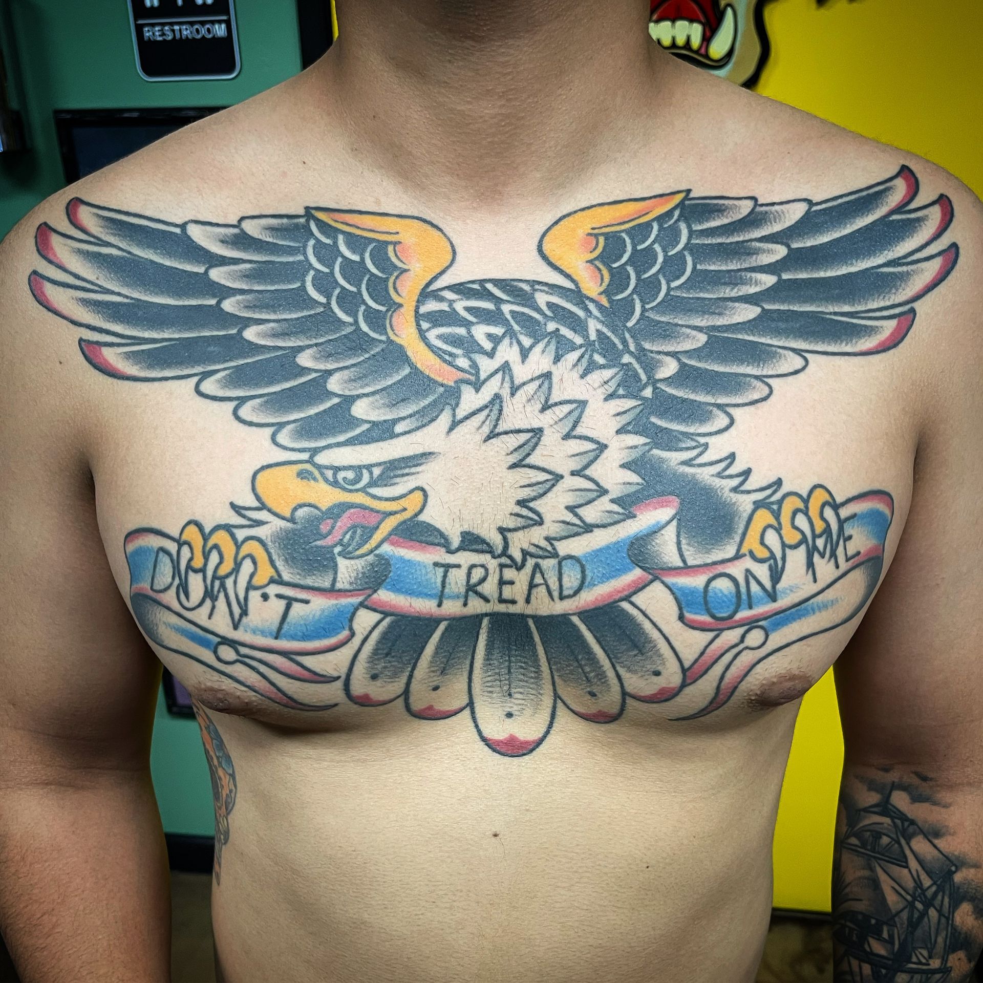 Tattoo of an eagle with outstretched wings and a banner that reads, 