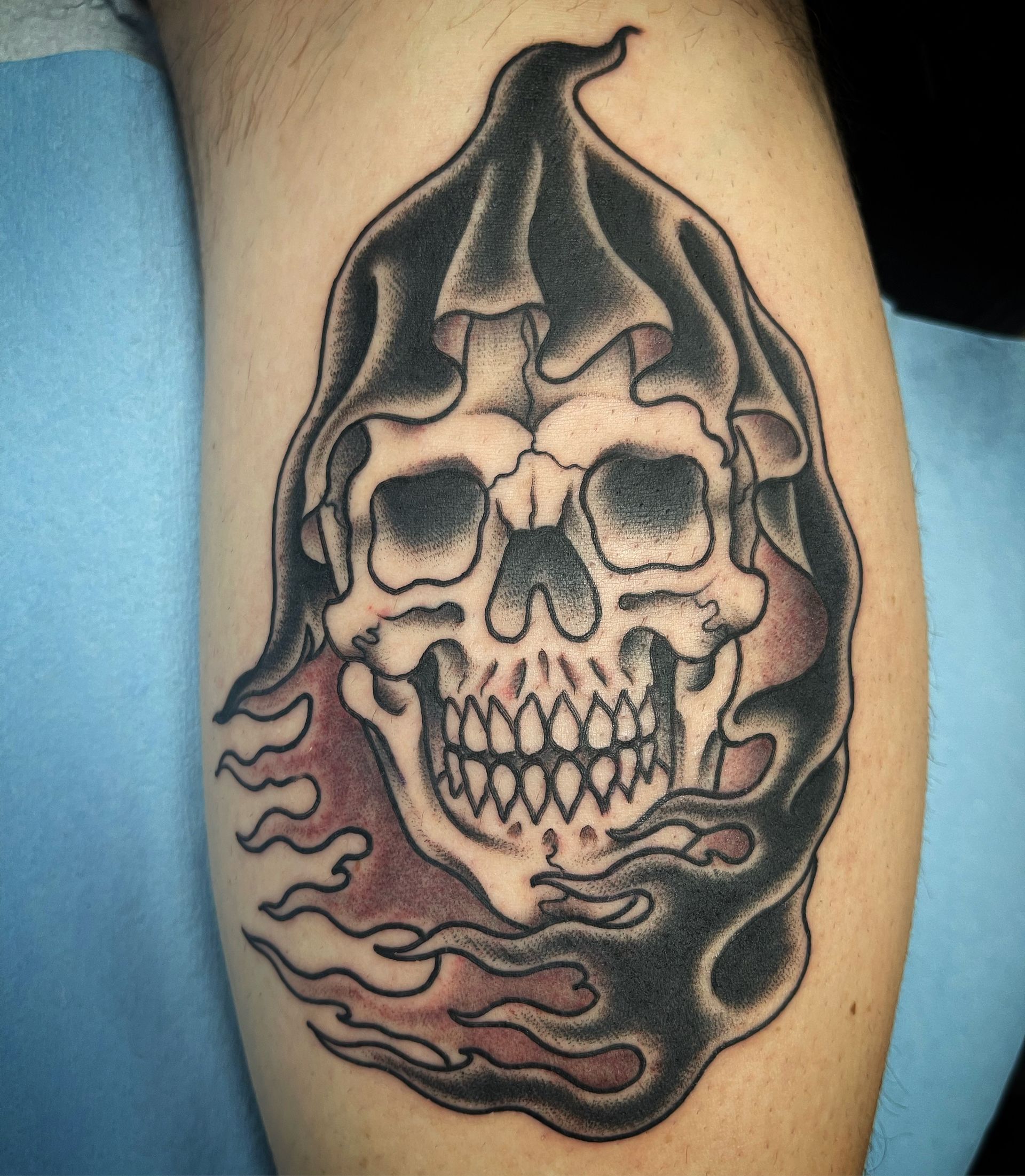 Grim Reaper skull tattoo, black cloak, red flames on skin.