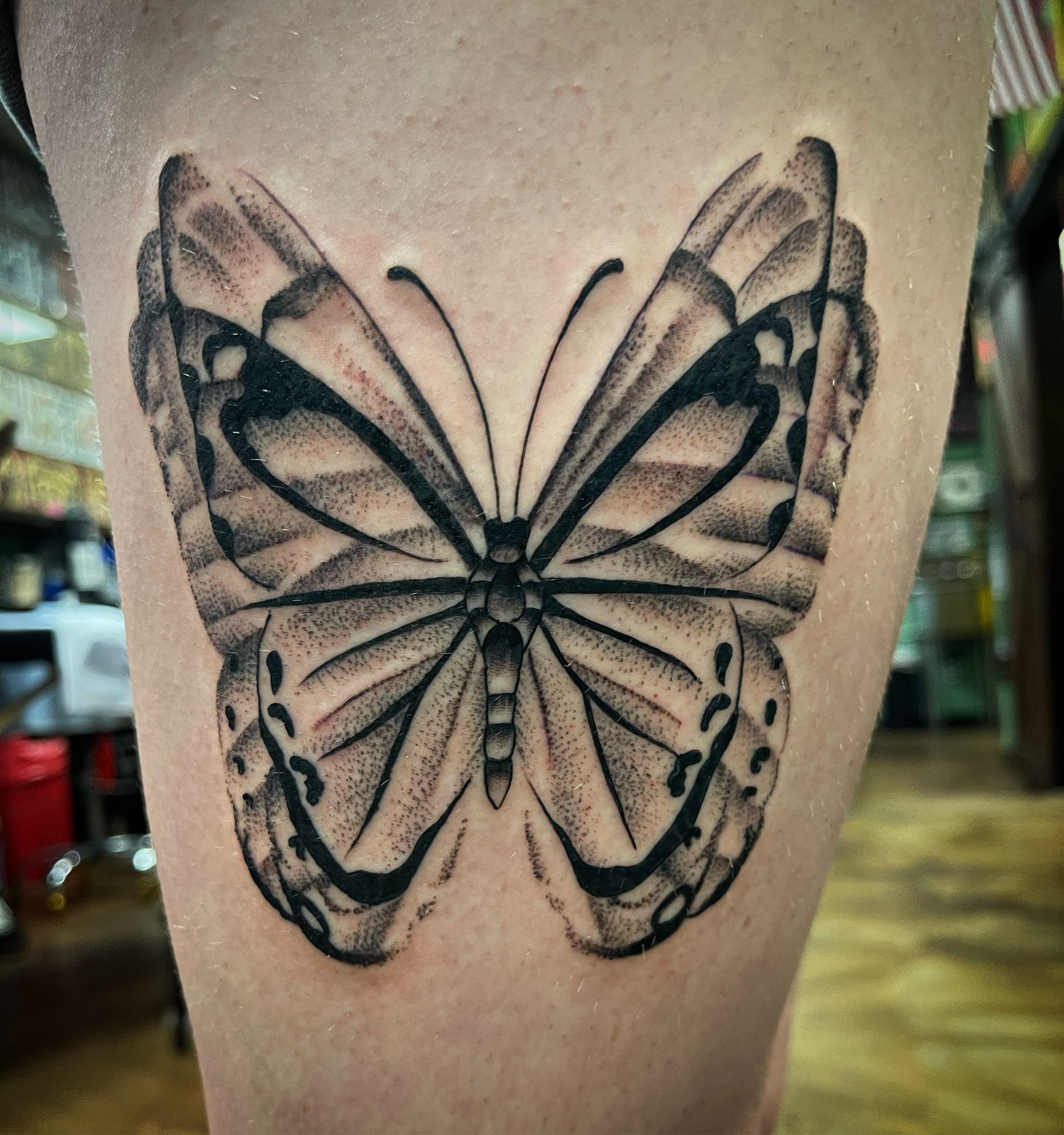 Black and gray butterfly tattoo on a leg. Wings detailed with dot work.