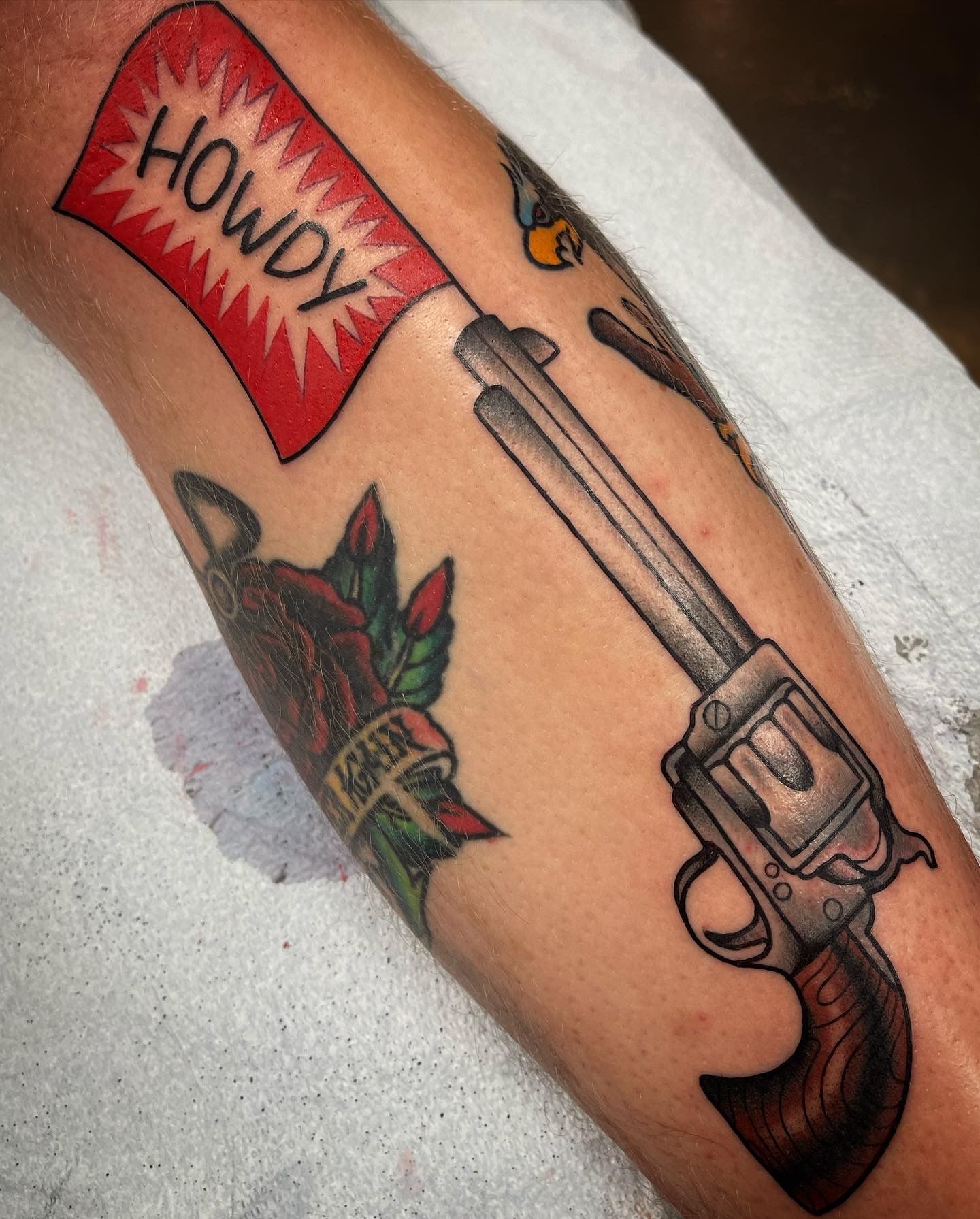 Tattoo on arm, a revolver with a red flag that says 