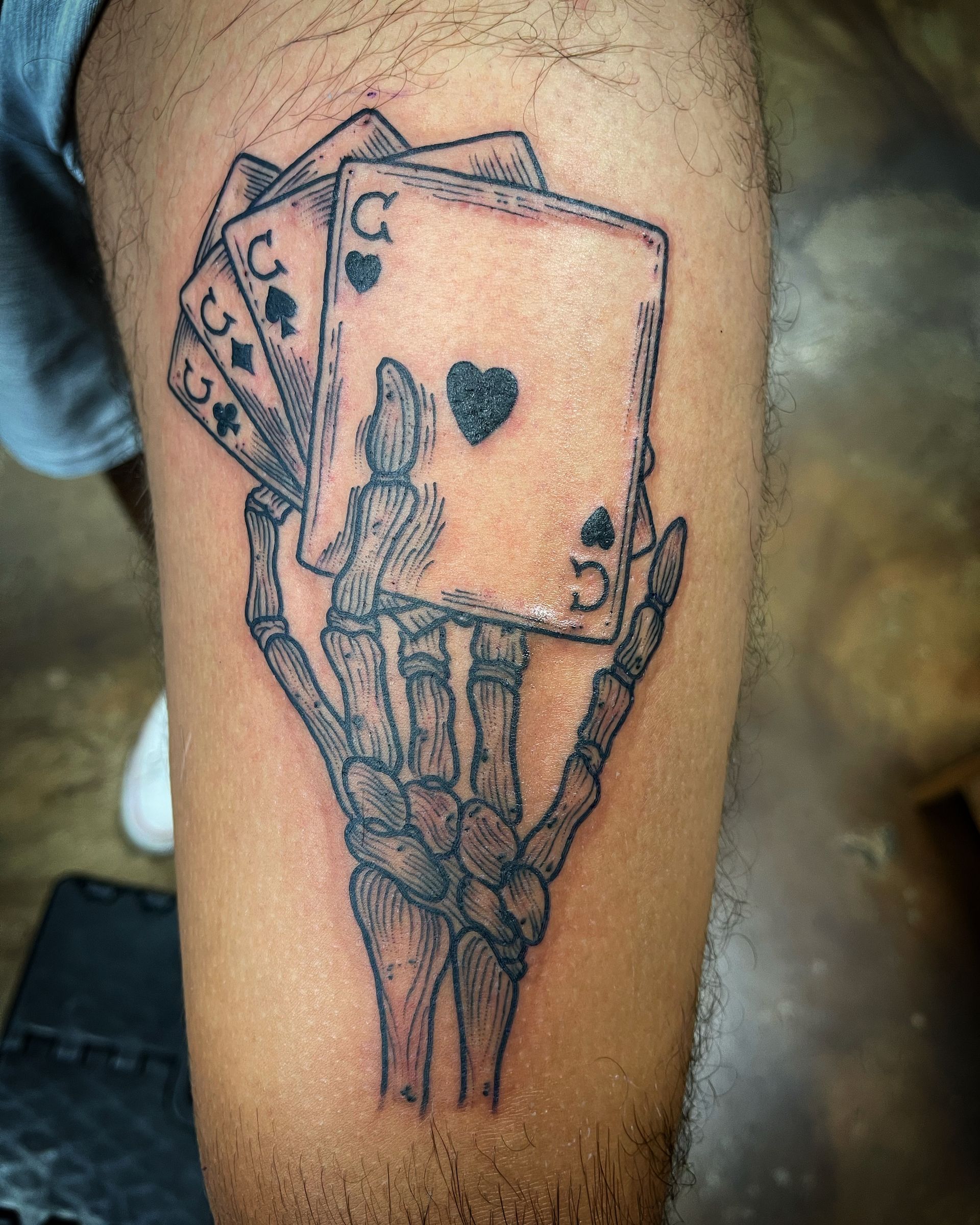 Tattoo on a leg: skeletal hand holding playing cards. Spade and club suits are visible.