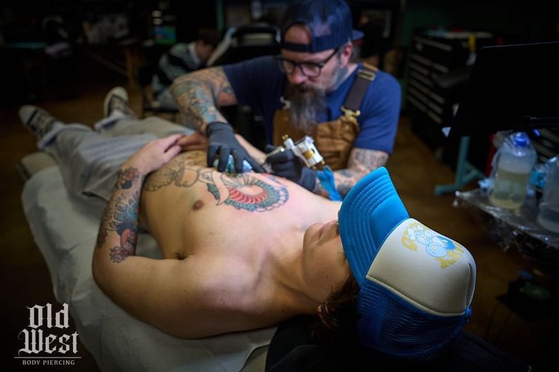 Tattoo artist in blue cap inks a design on a person's chest. Studio setting, artist and client focused.