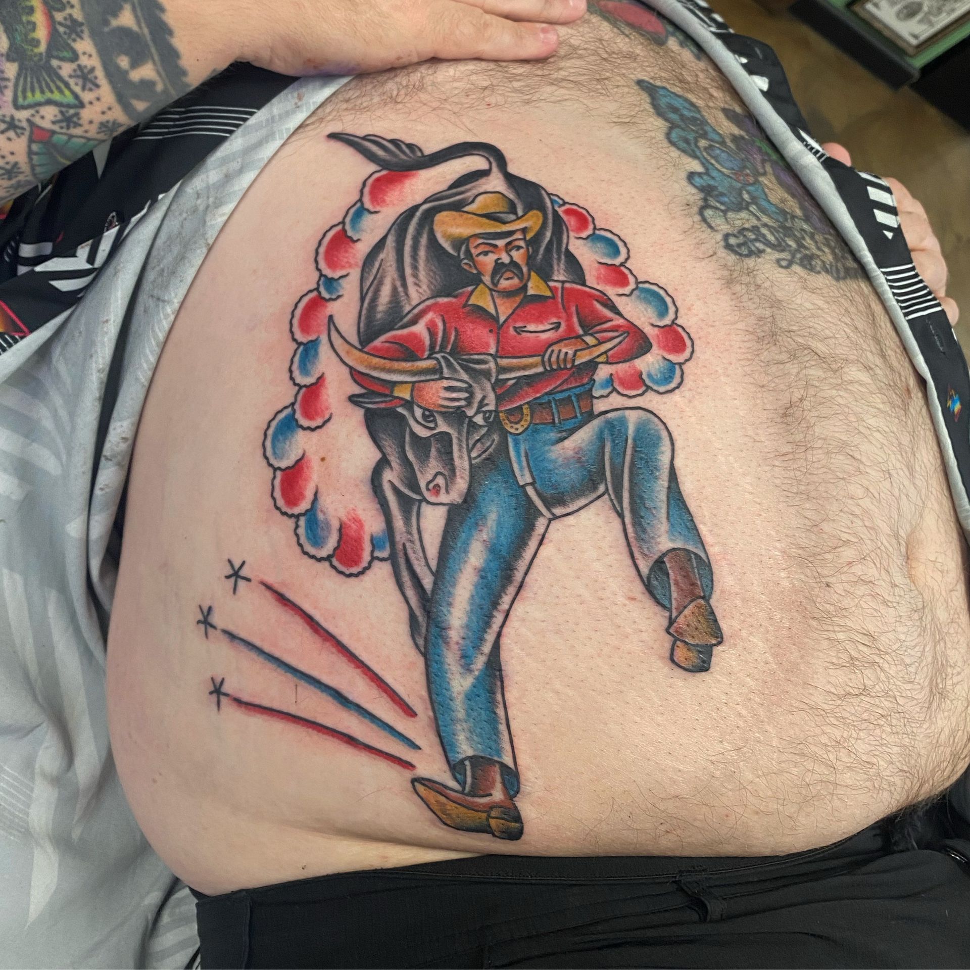 Tattoo of a cowboy riding a bull, with red, blue, and black ink.
