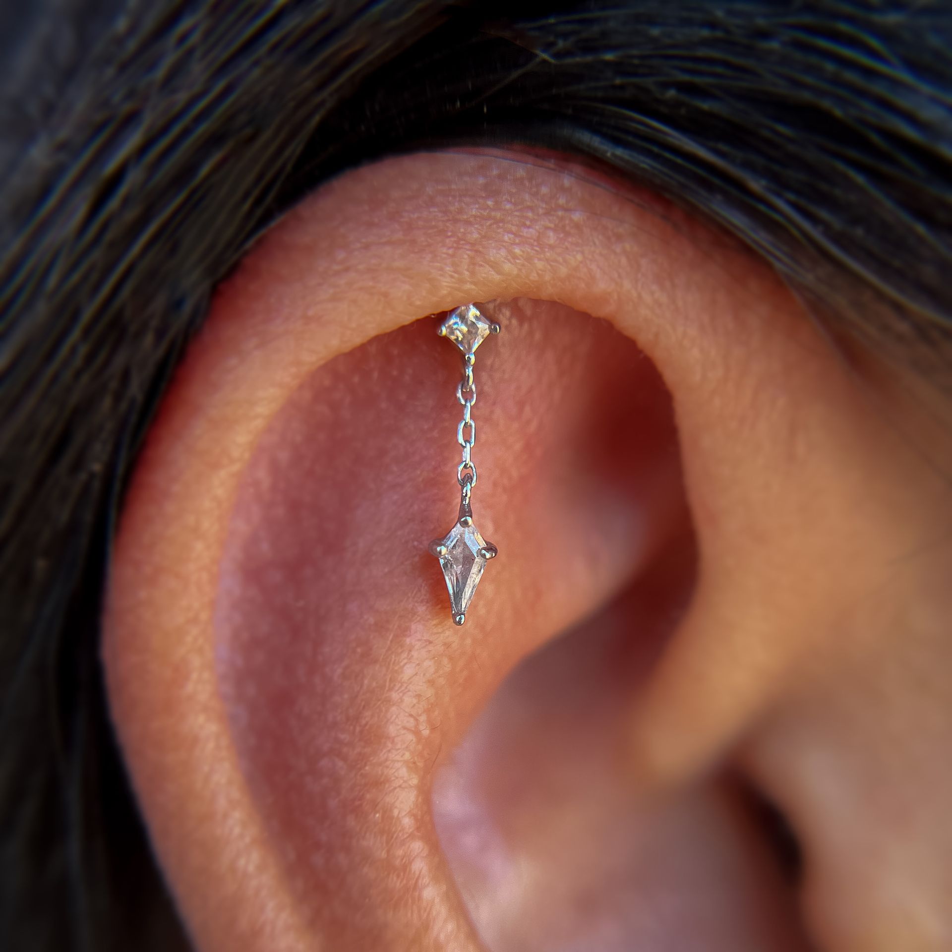 Close-up of an ear wearing a delicate silver dangling earring.