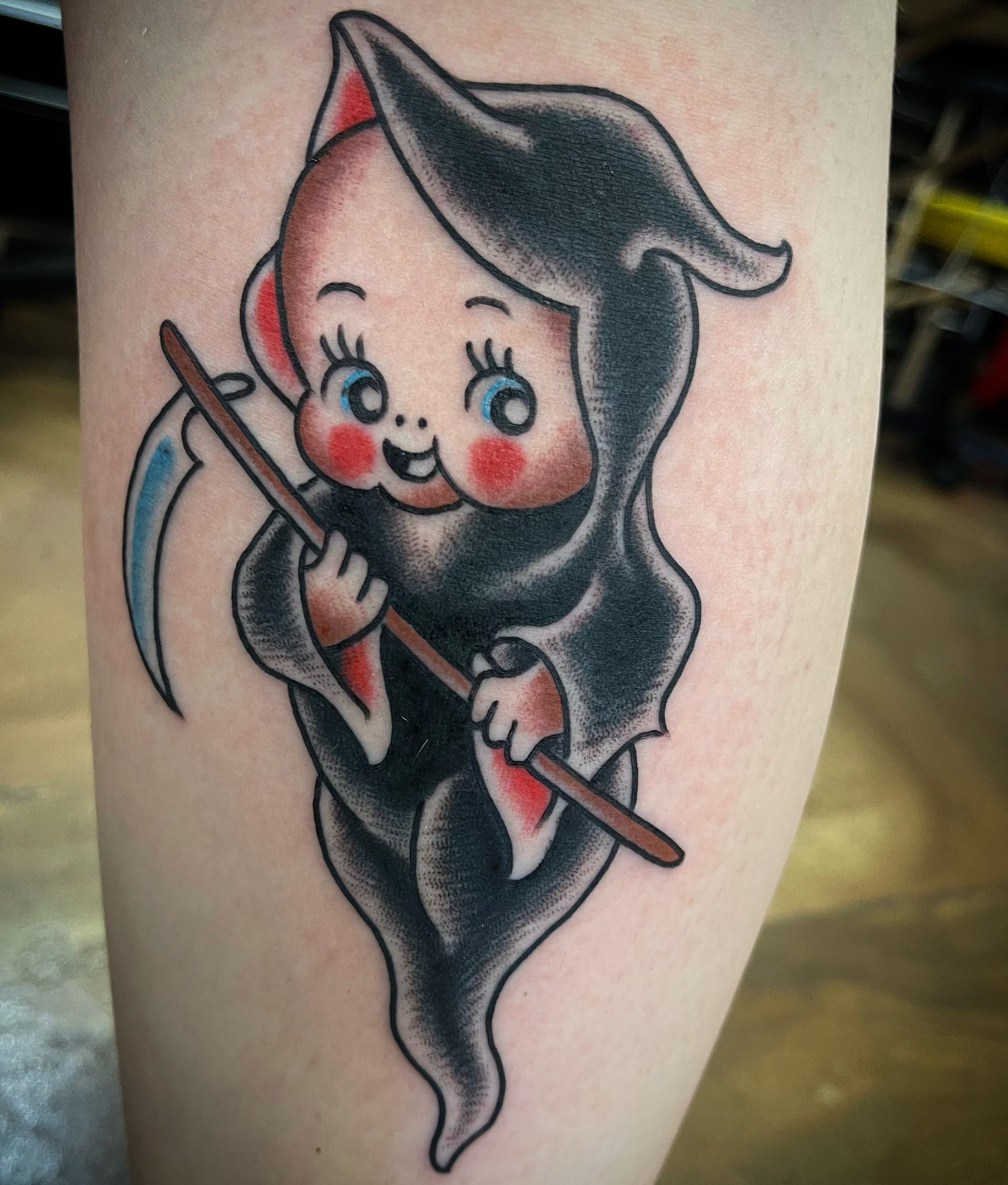 Cartoonish grim reaper with a scythe, dressed in black, with rosy cheeks and a happy expression.
