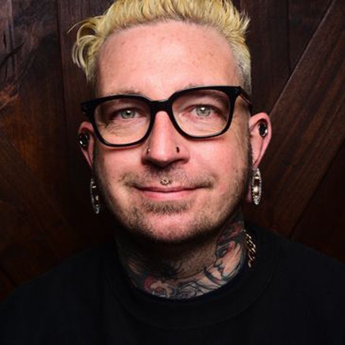 The man is wearing glasses and earrings and has a tattoo on his neck.
