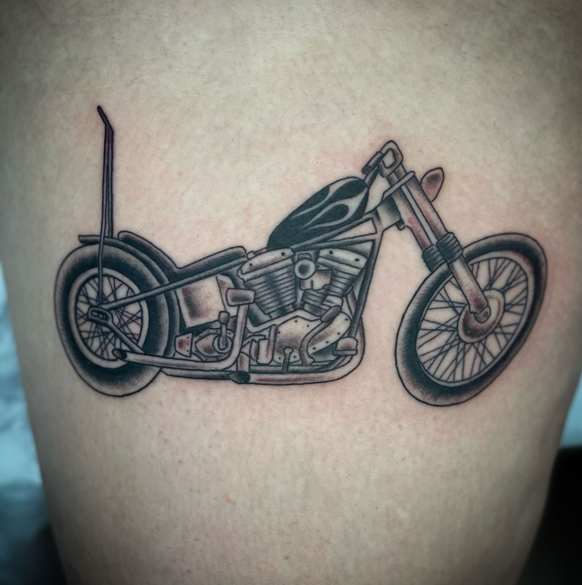 Black and gray tattoo of a chopper motorcycle with a flame design on the gas tank.