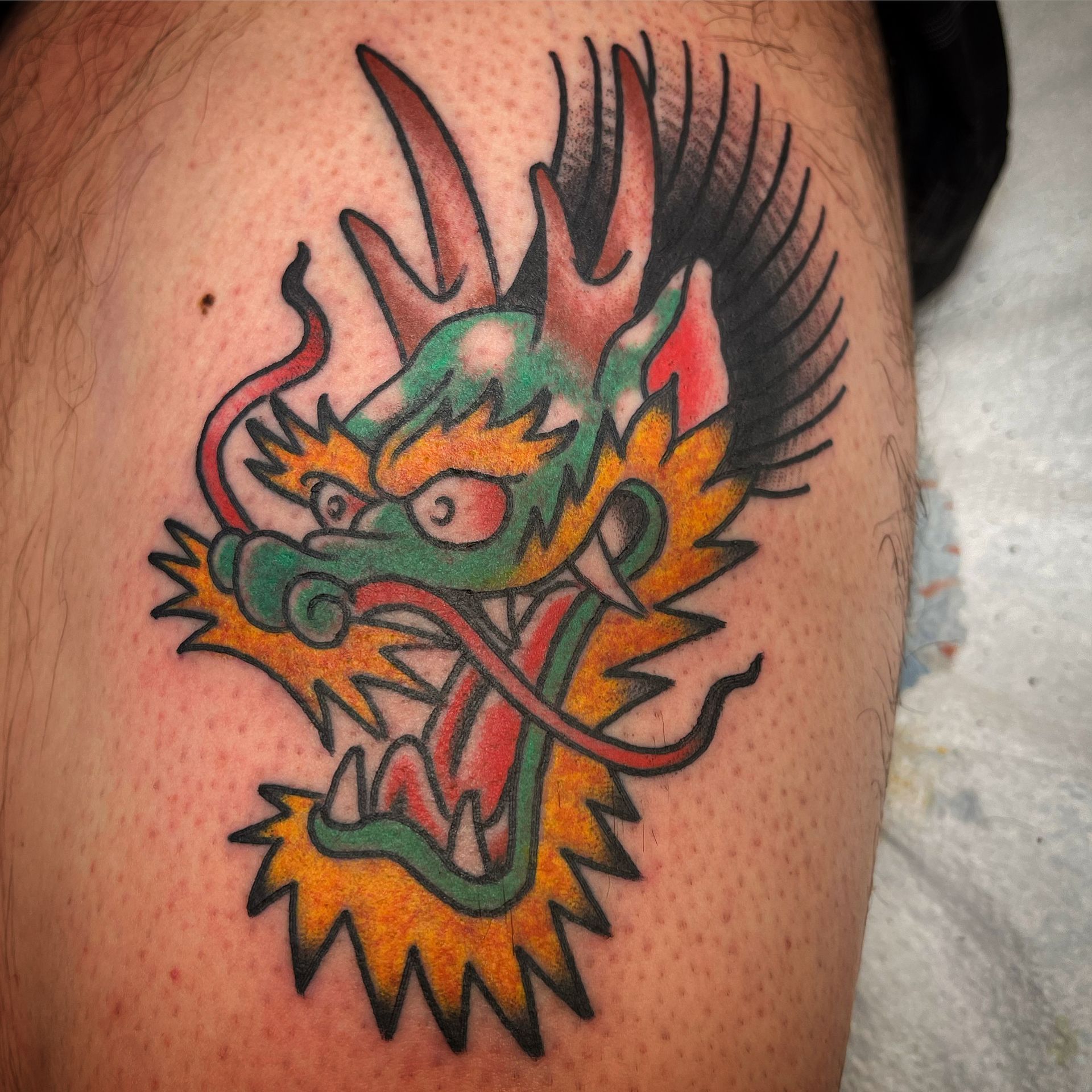 Dragon tattoo on skin, green head with yellow and orange details, red eyes and open mouth.