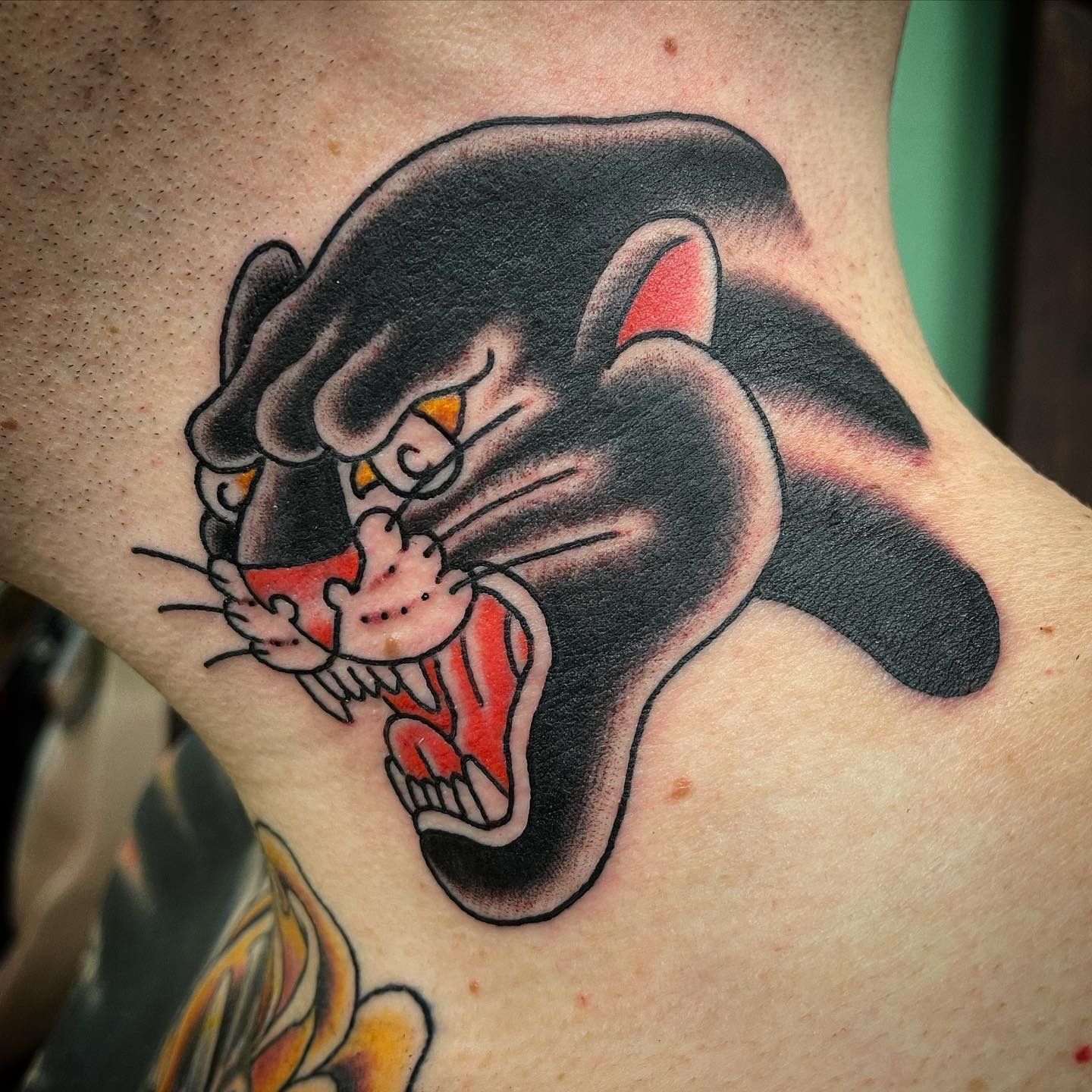 Black panther tattoo on a neck, roaring, with red mouth and yellow eyes.