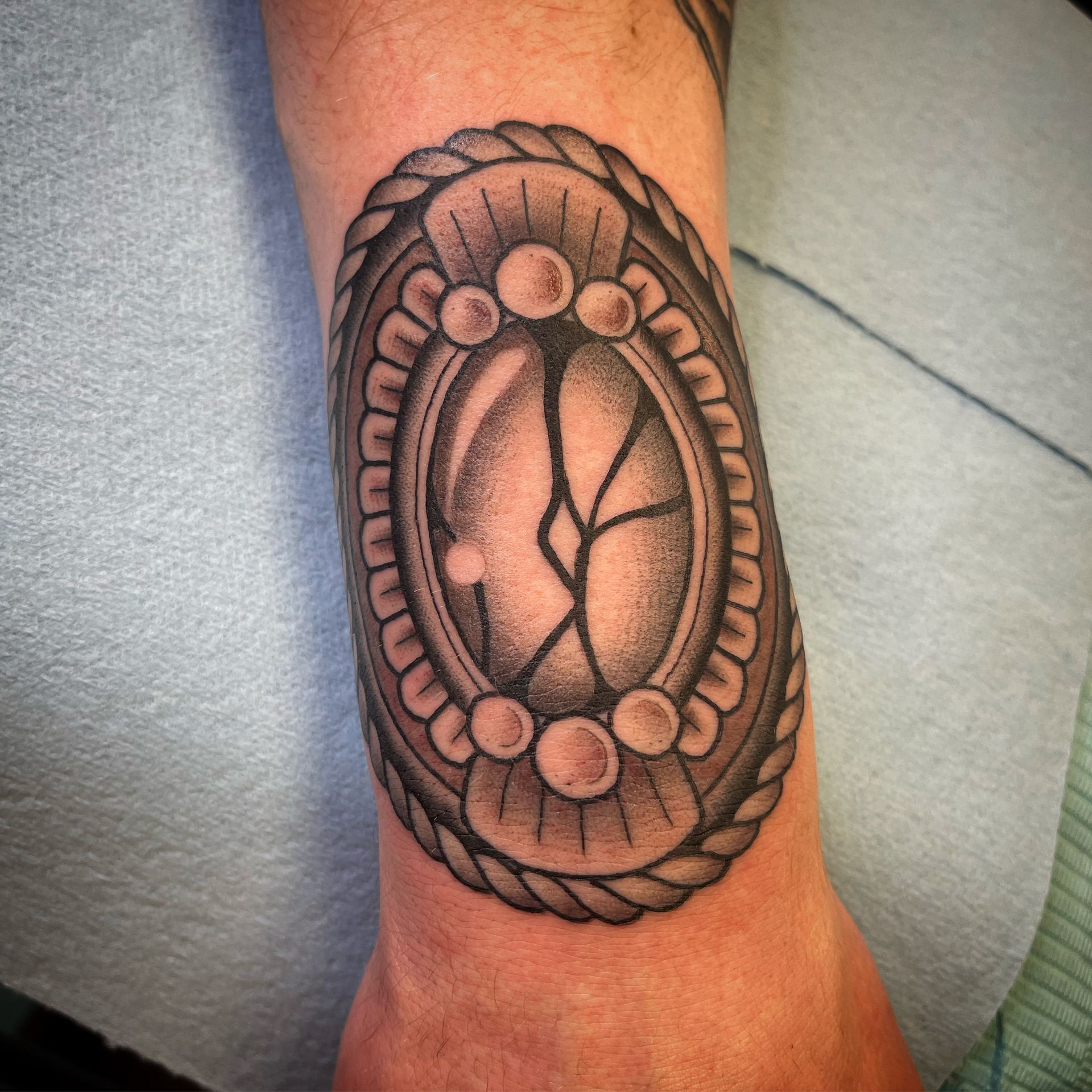 Tattoo on wrist: oval mirror with cracks, surrounded by rope and pearl-like beads.