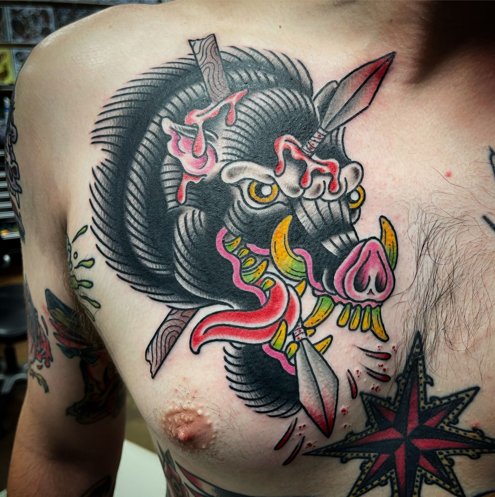 Tattoo of a wild boar with spears, black fur, pink snout, and blood, on a person's chest.