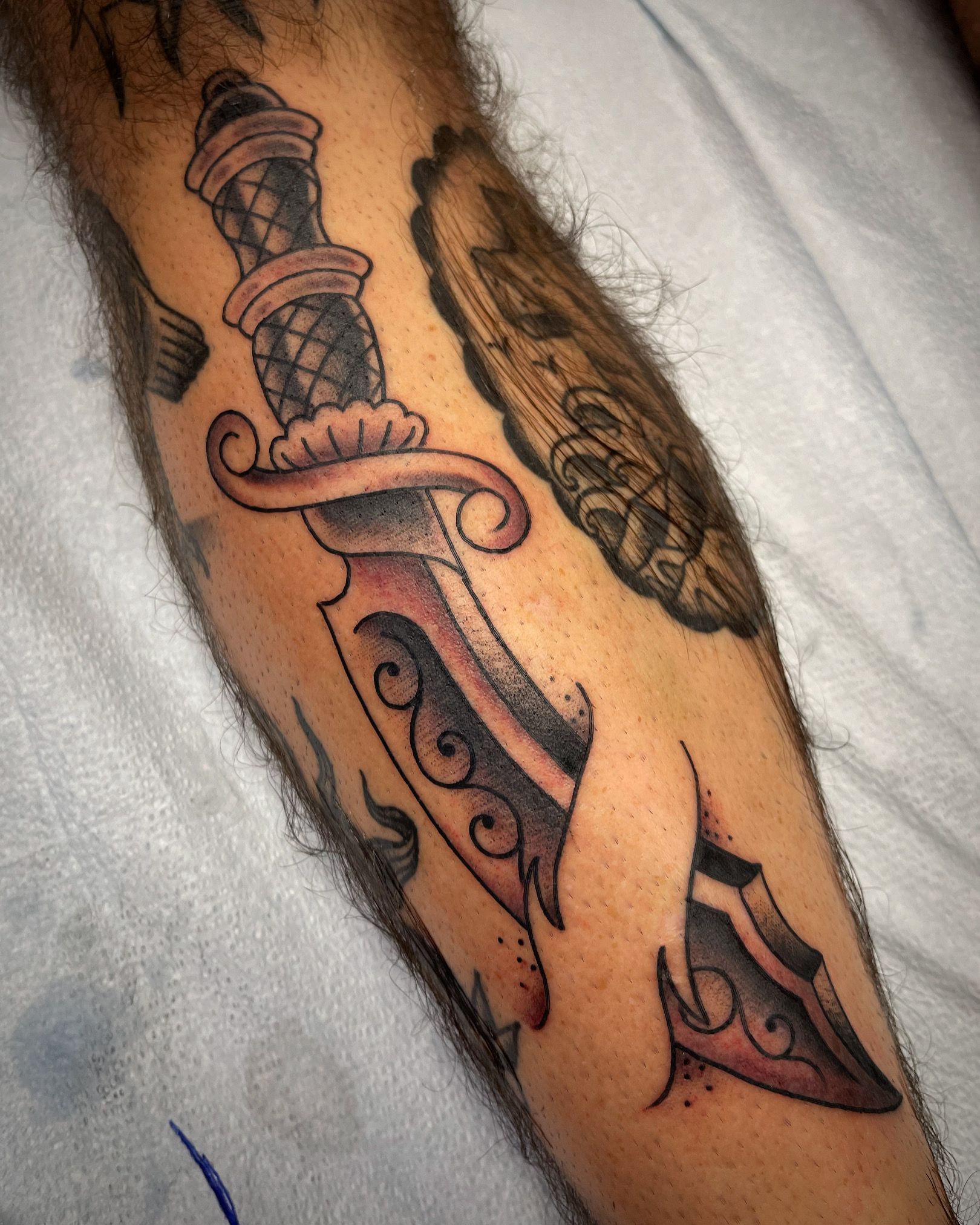Tattoo of a dagger with ornate handle and blade, on a person's arm.