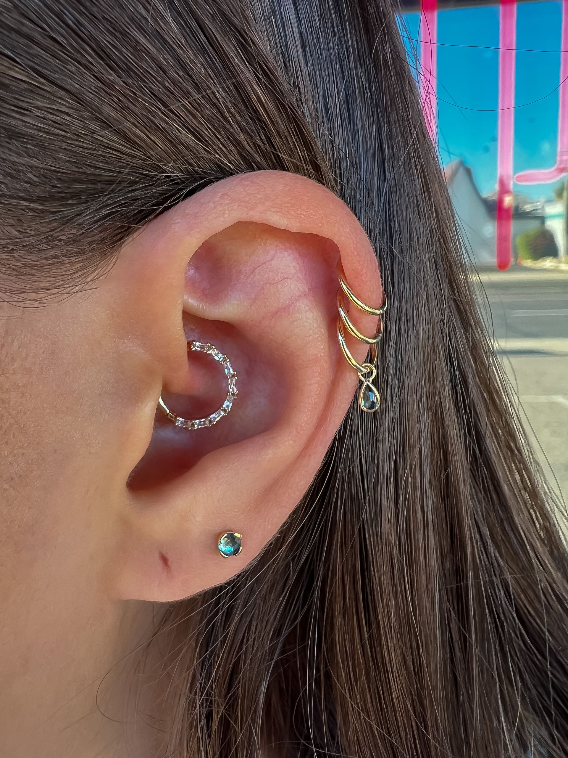 Close-up of an ear with multiple gold hoop earrings and a turquoise stud earring outside.