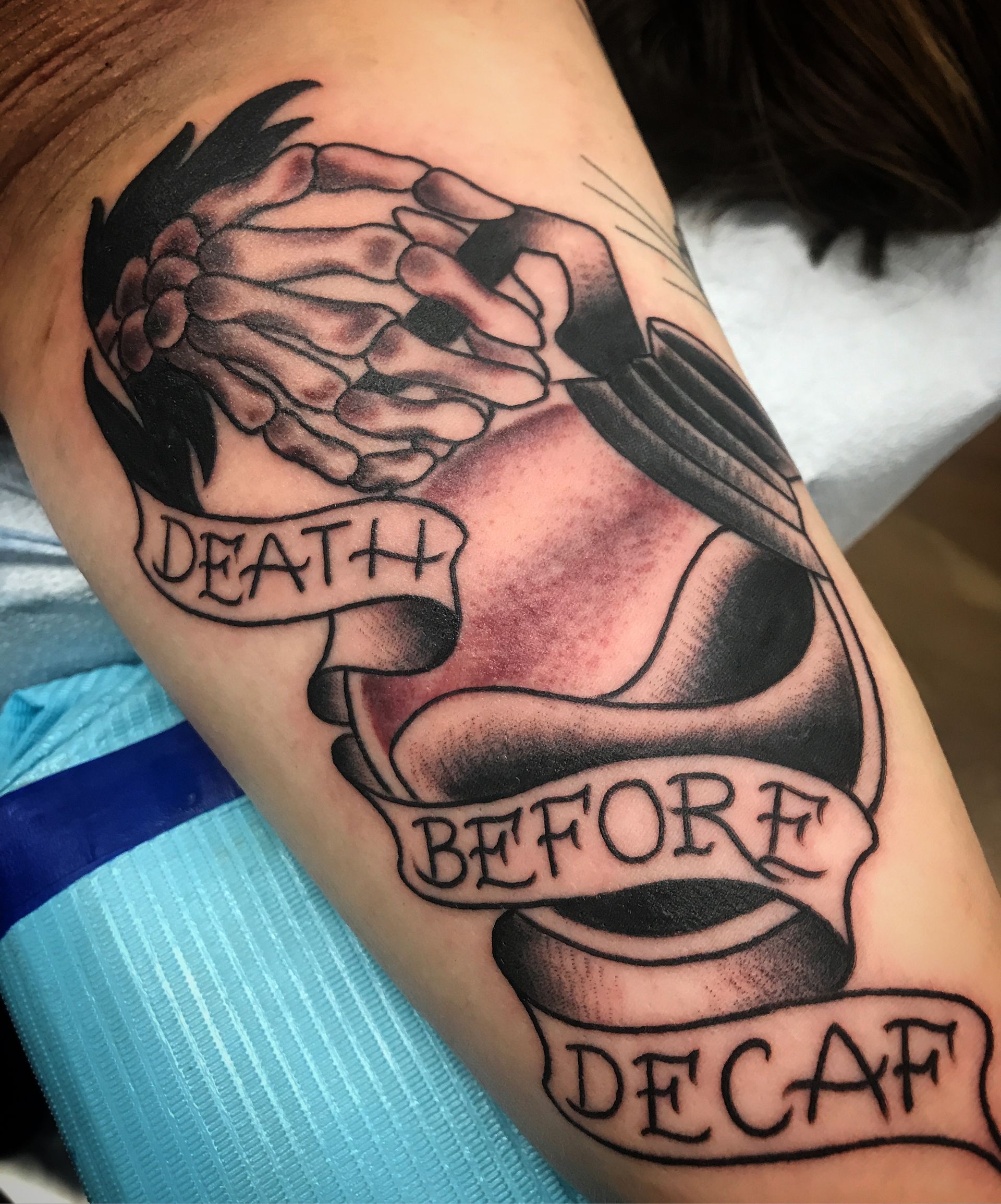 Tattoo on arm: skeletal hand covers eyes above banner reading 