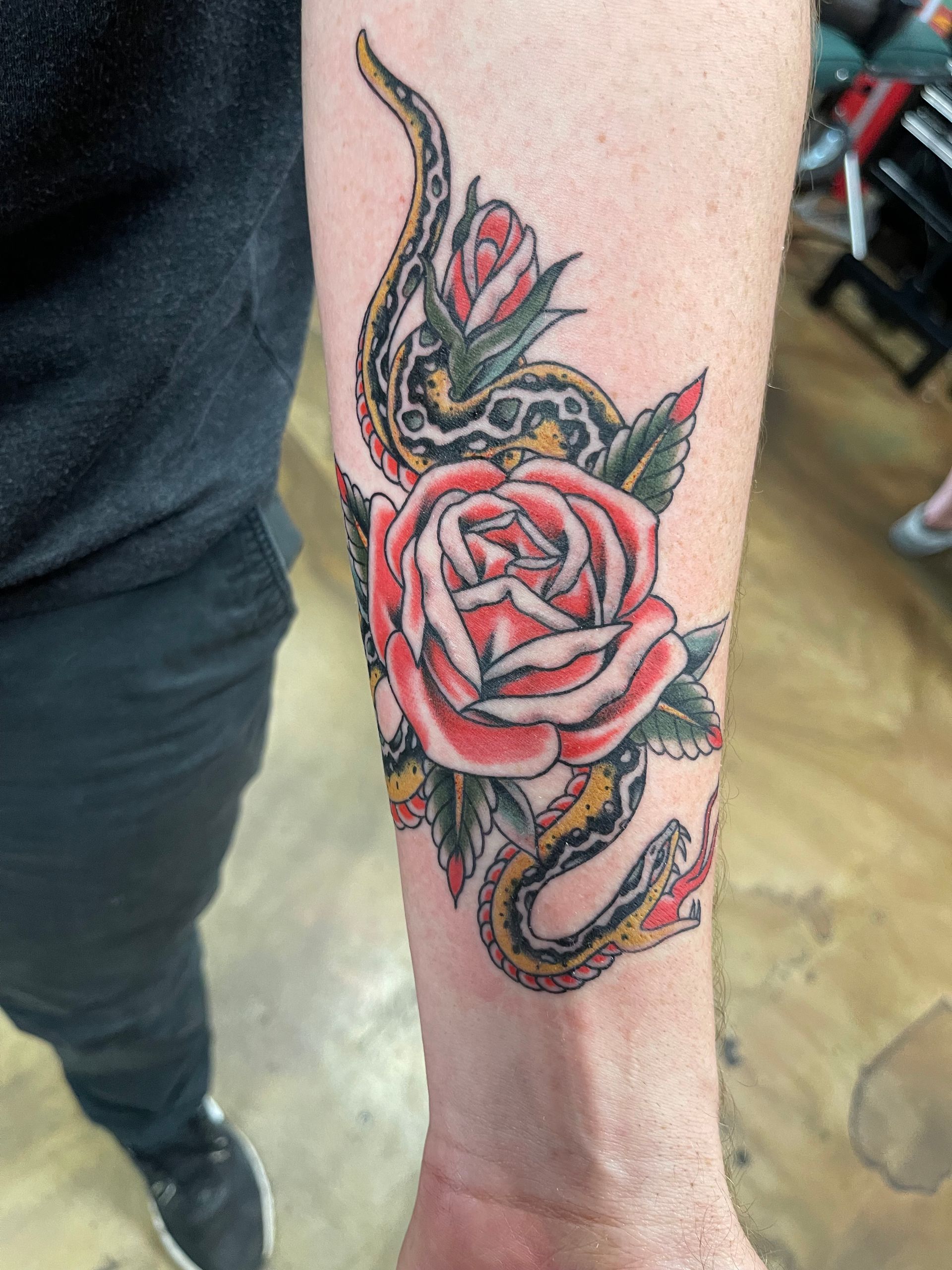 Tattoo of a snake wrapped around a red rose on a person's forearm.