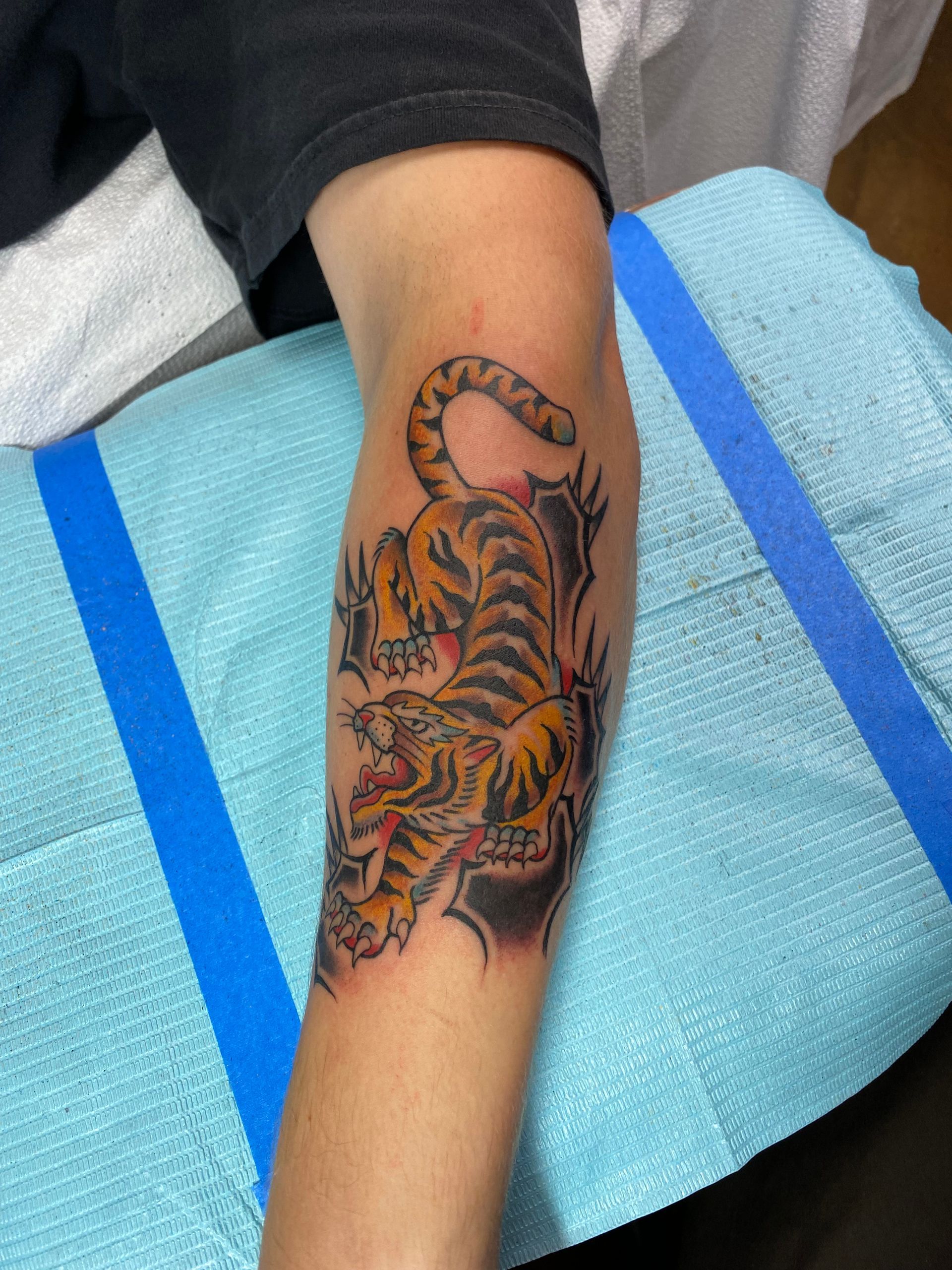 Arm with tiger tattoo, black and yellow, against a black background.