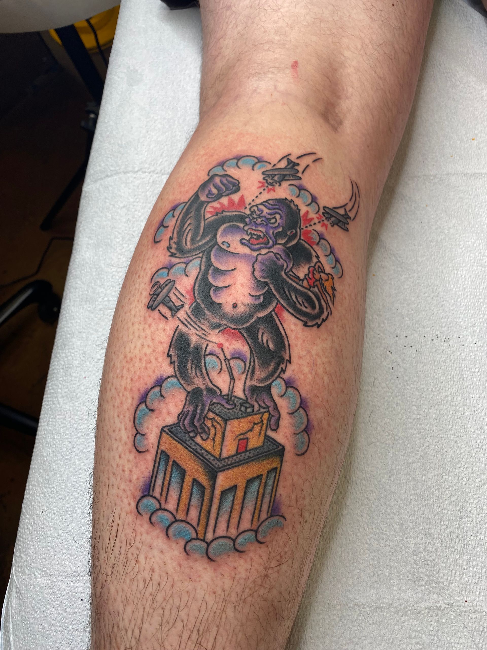 Tattoo of a gorilla atop a pedestal. Gray and black, with red accents. Gray leg.