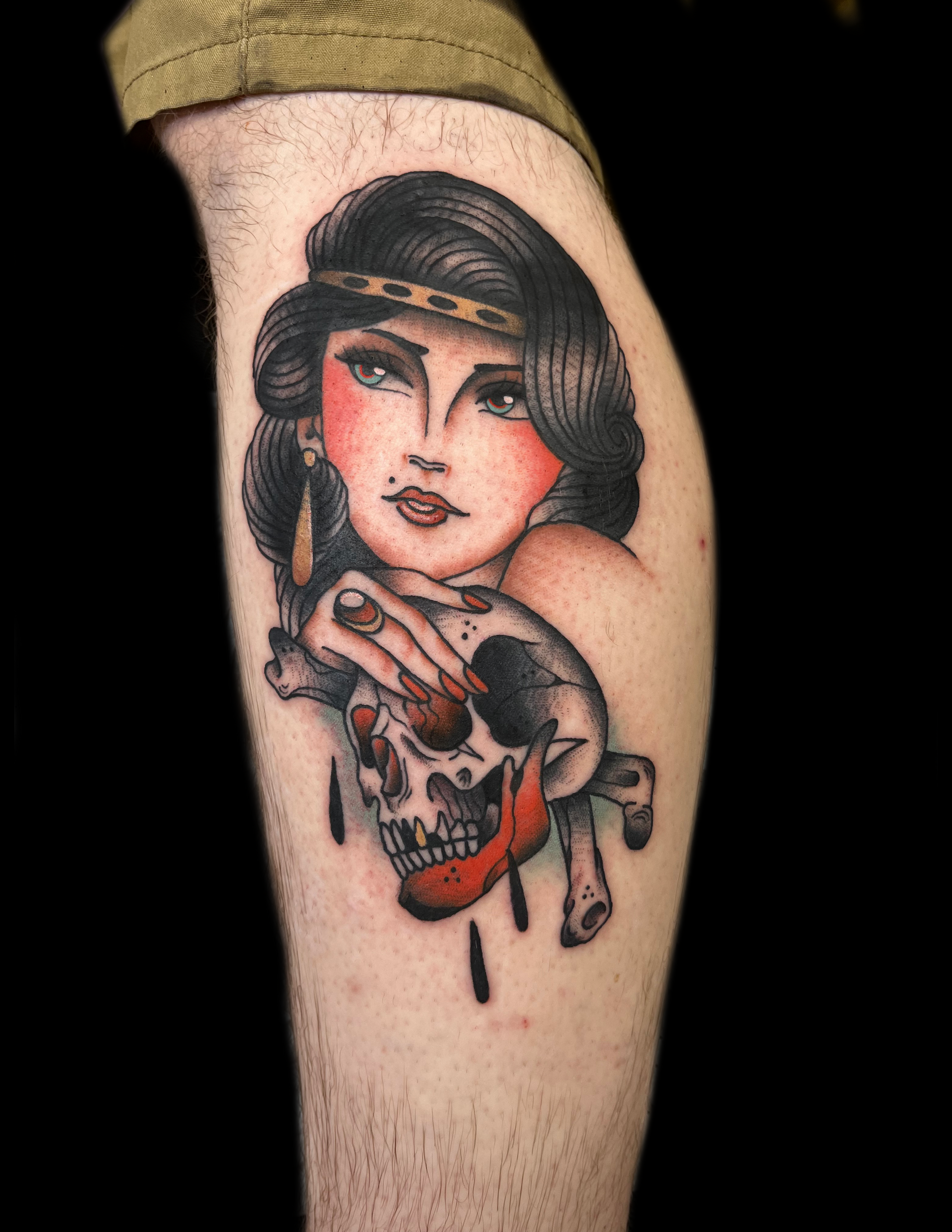 Tattoo of woman holding skull, red lipstick, black hair, headband, and dangling earrings.