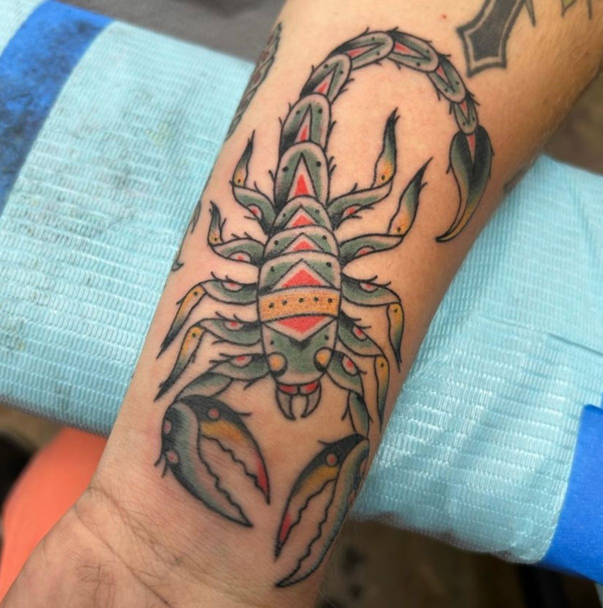 Traditional tattoo of a scorpion in green, red, and yellow on a person's wrist.