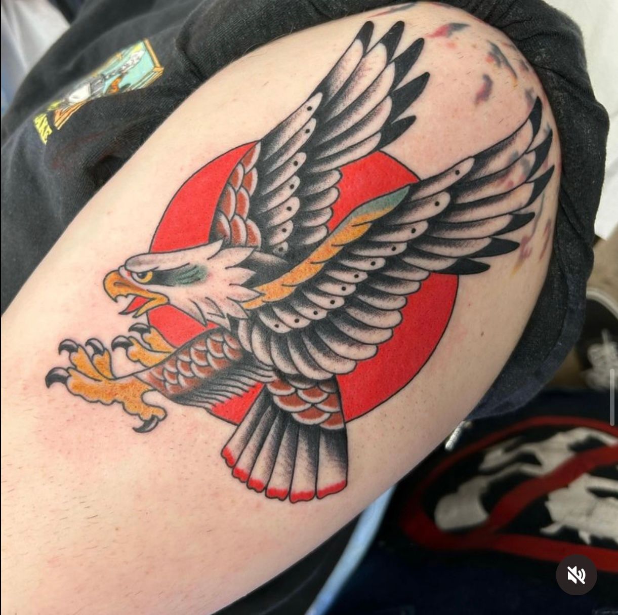 Tattoo of an eagle in flight with a red sun background. The eagle has outstretched wings, an open beak, and yellow talons.