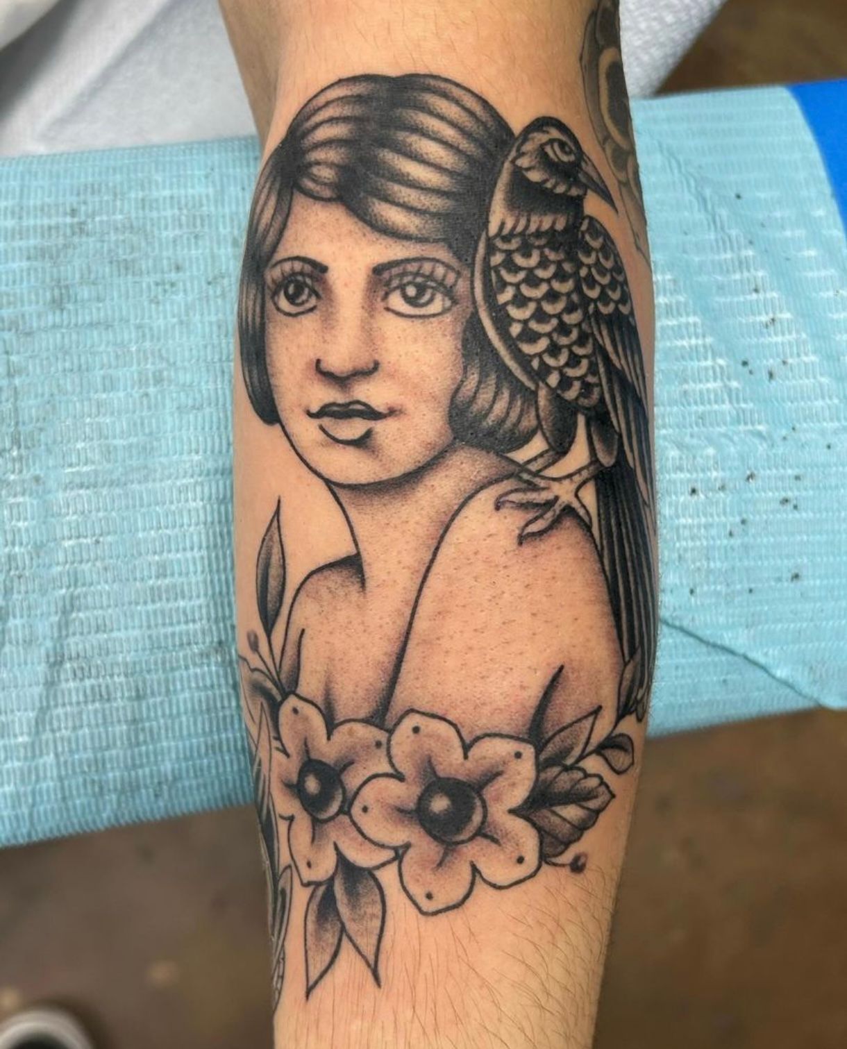 Tattoo of a woman with a bird perched on her shoulder, flowers at her chest; black and white.