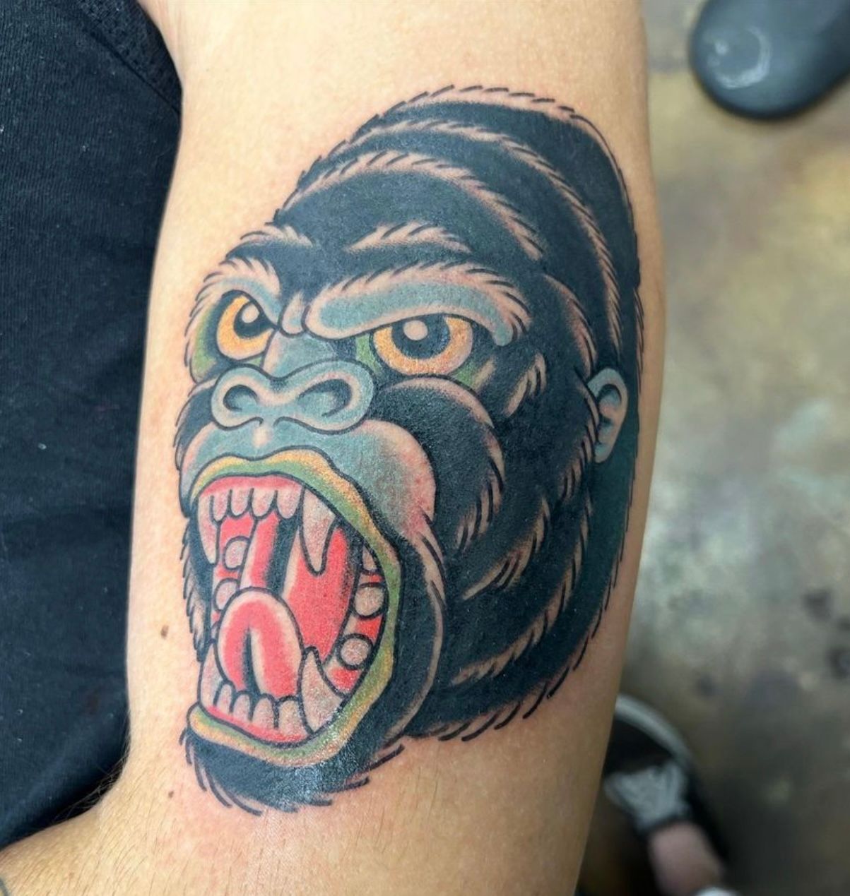 Tattoo of an angry gorilla head with open mouth on a person's arm, traditional style, black, blue, and red.