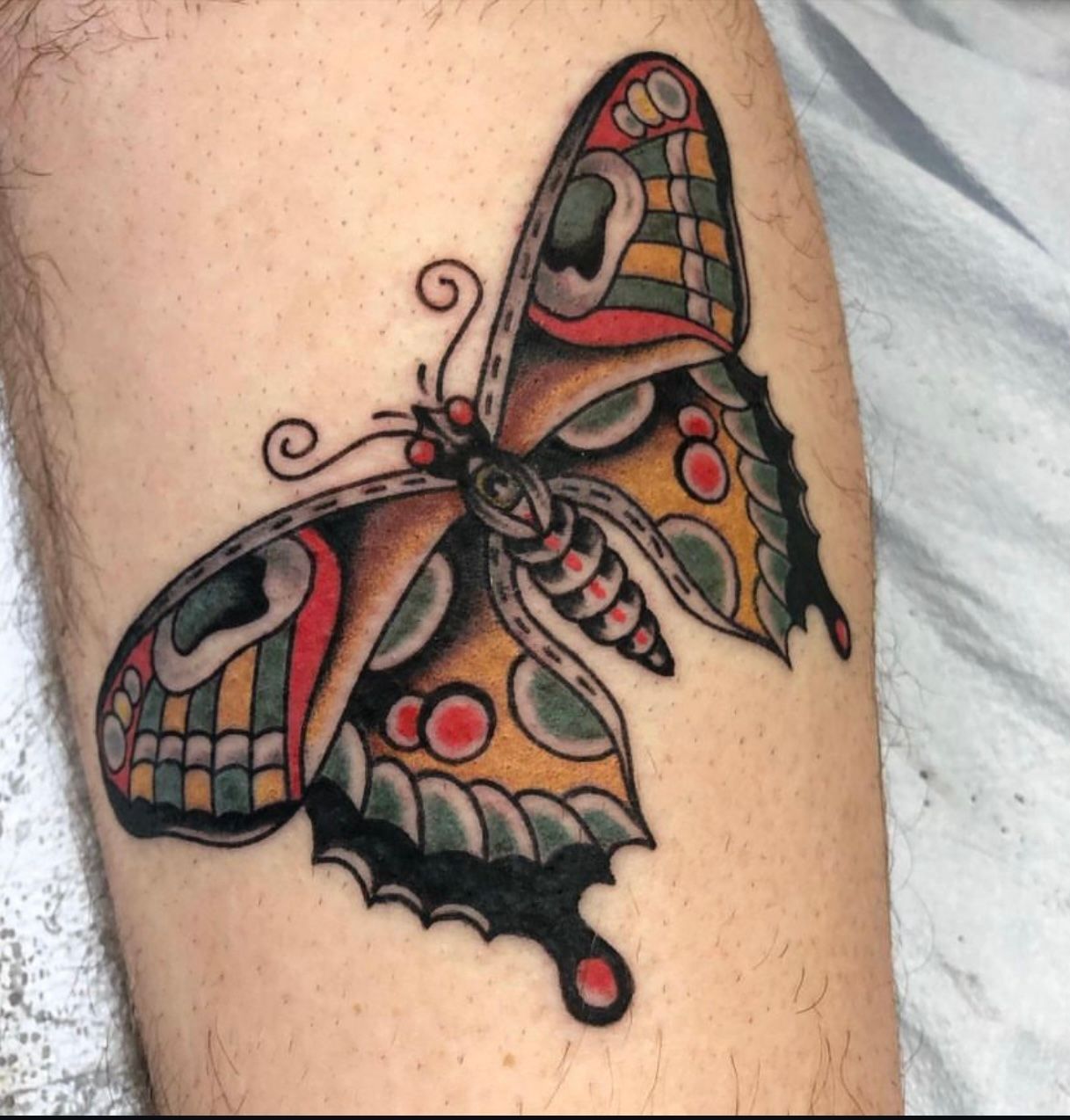 Traditional style butterfly tattoo on a leg. Yellow, red, green, black details.