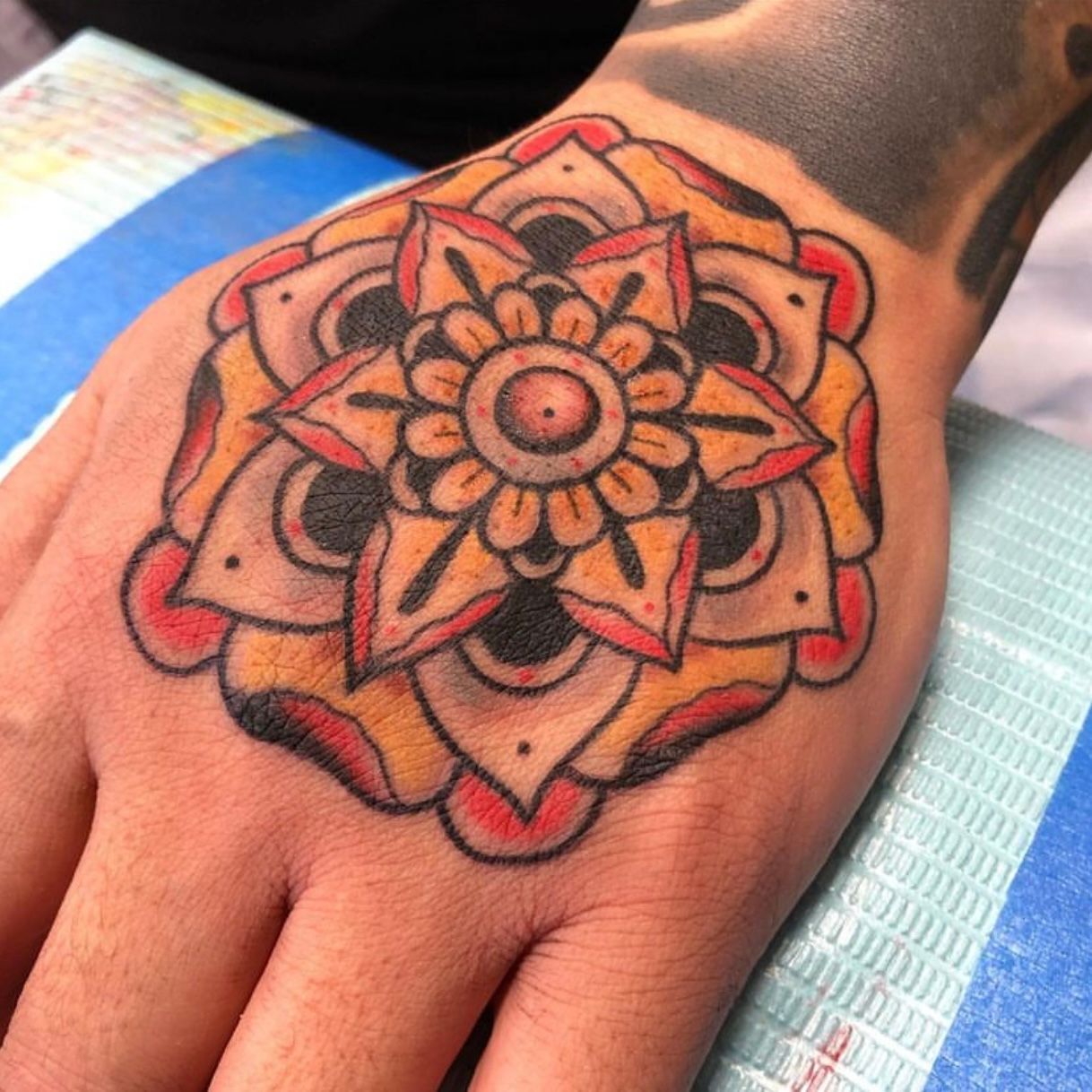 Hand tattoo of a colorful floral design with black, yellow, and red details.