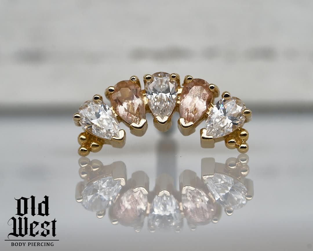 Gold ring with pear-shaped gems in a curved row, with a reflected image below.
