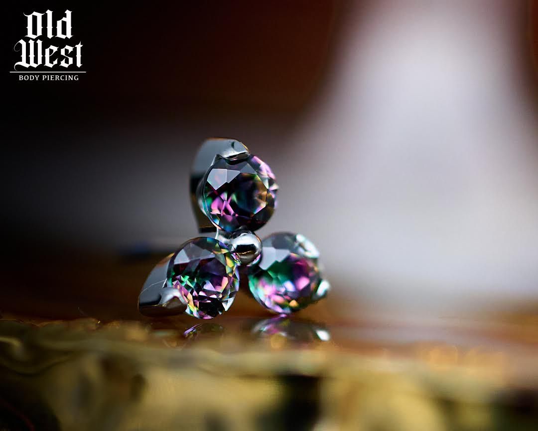 A close-up of a silver, three-gemstone stud earring with iridescent crystals, set against a blurred background.