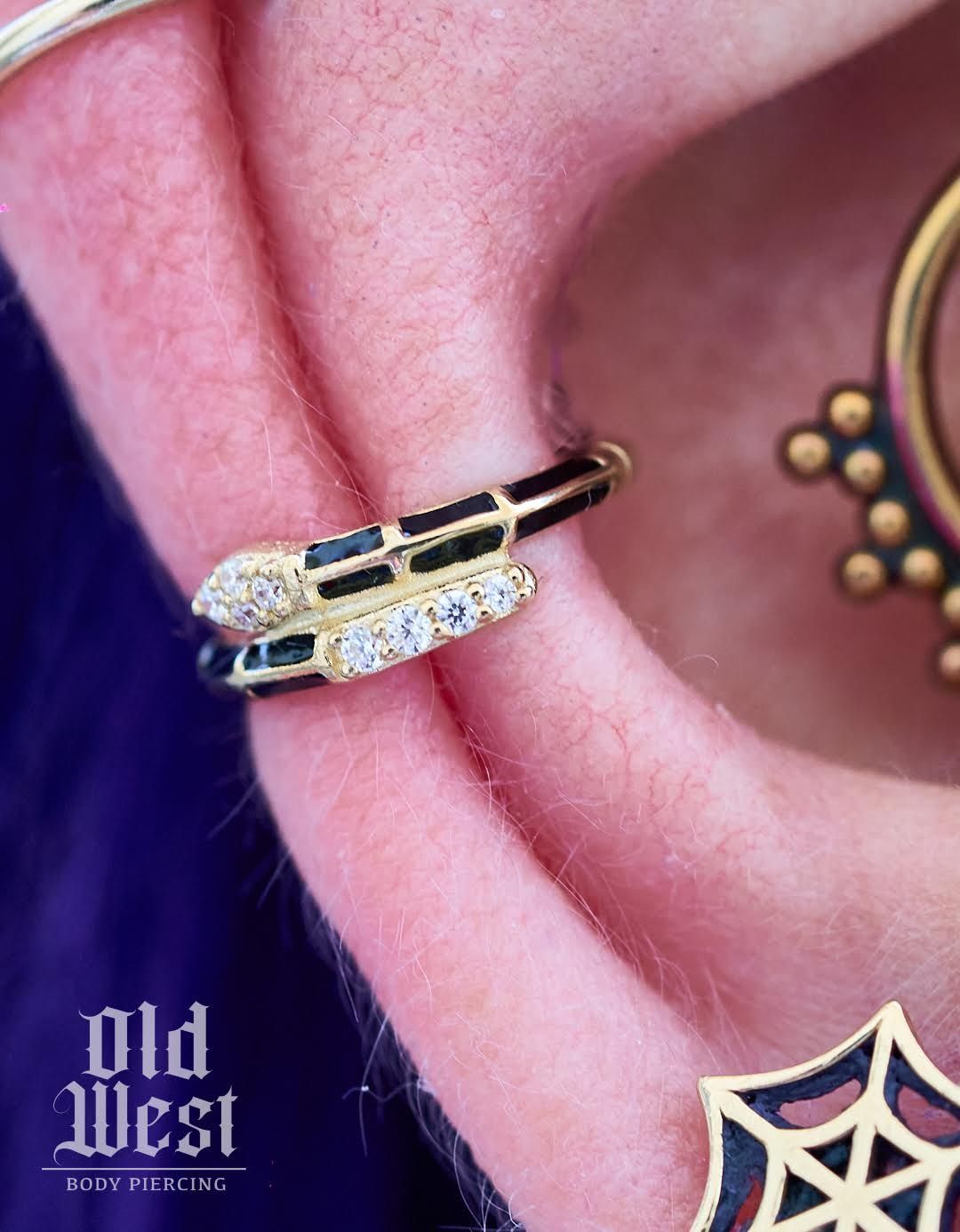 Gold snake ear piercing with black enamel and clear stones.