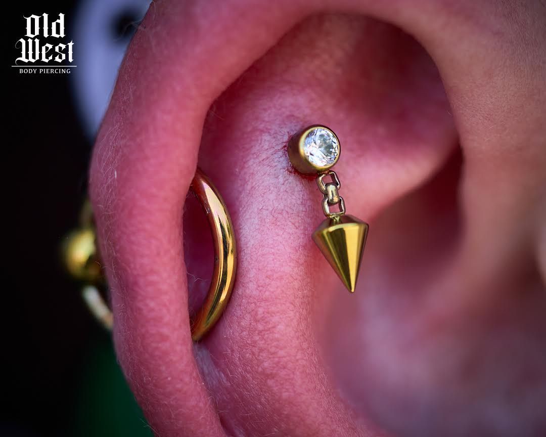 Close-up of ear with a gold helix ring and a forward helix piercing with a charm.