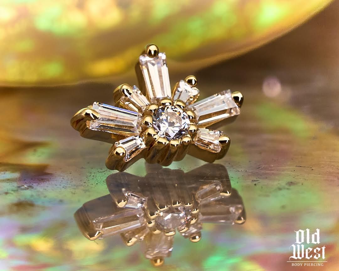 Gold flower-shaped piercing with a central white gem and baguette-cut stones.