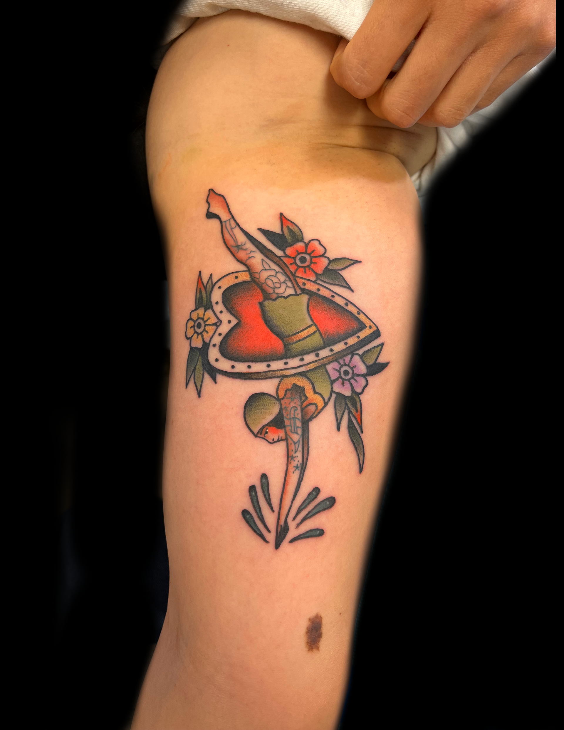 Tattoo of a dagger piercing a heart with flowers; on a thigh.