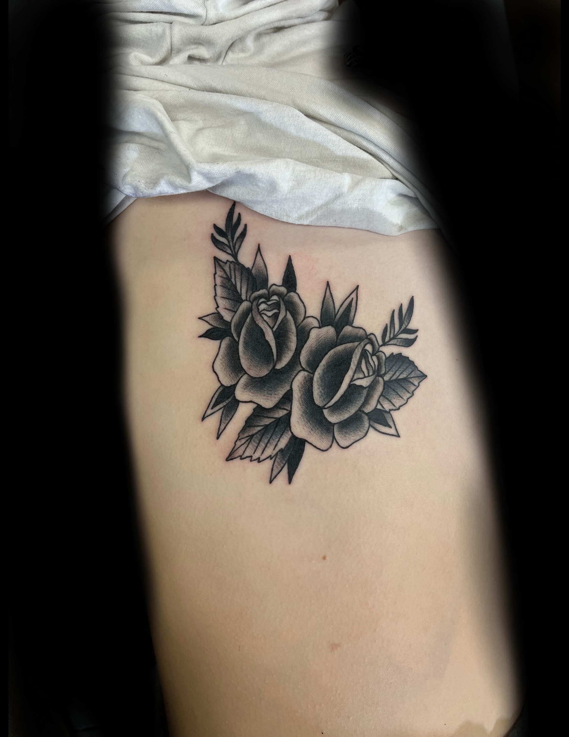 Black and white rose tattoo on a person's side, showing two roses with leaves.