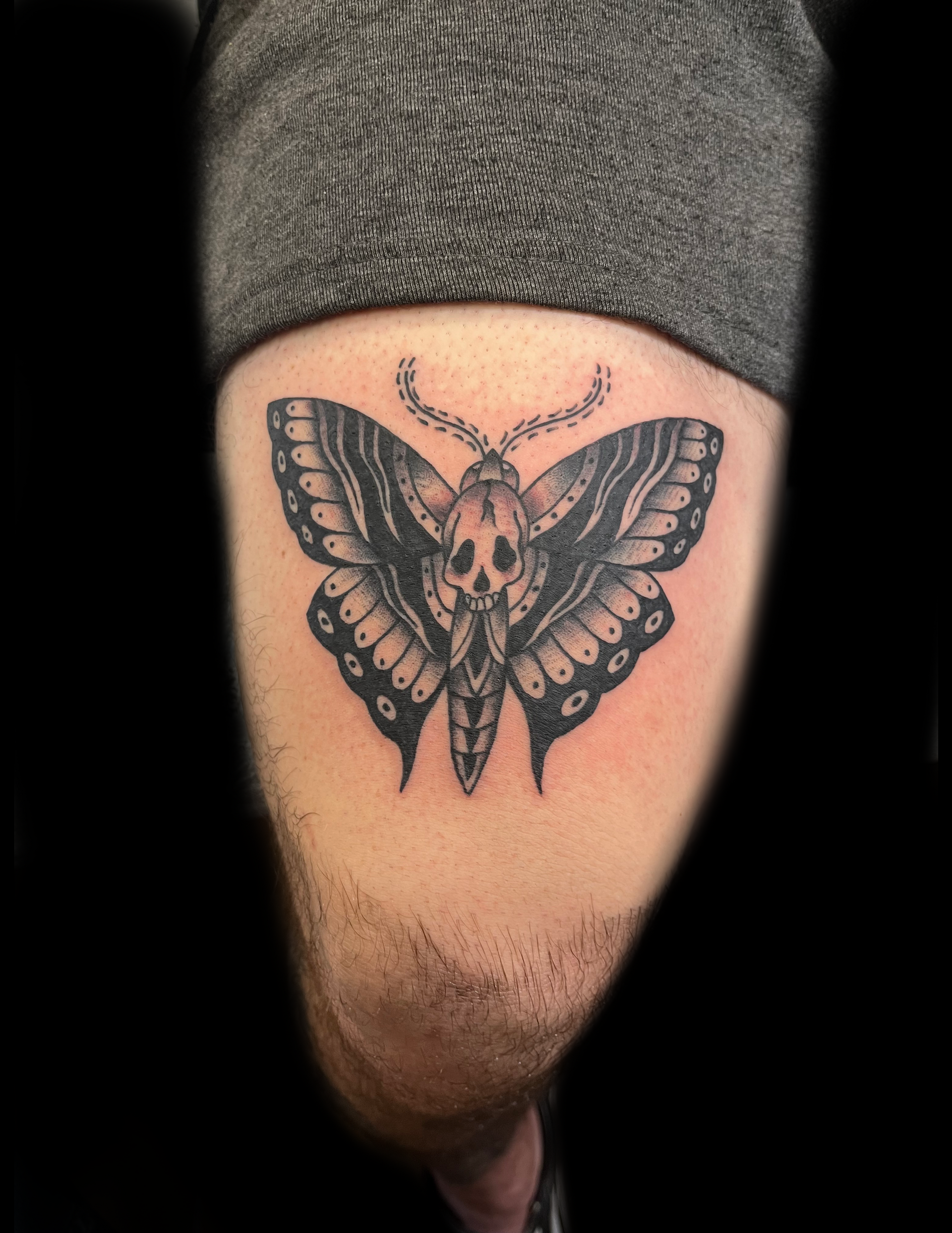 Tattoo of a black and gray Death's-head moth on a thigh.