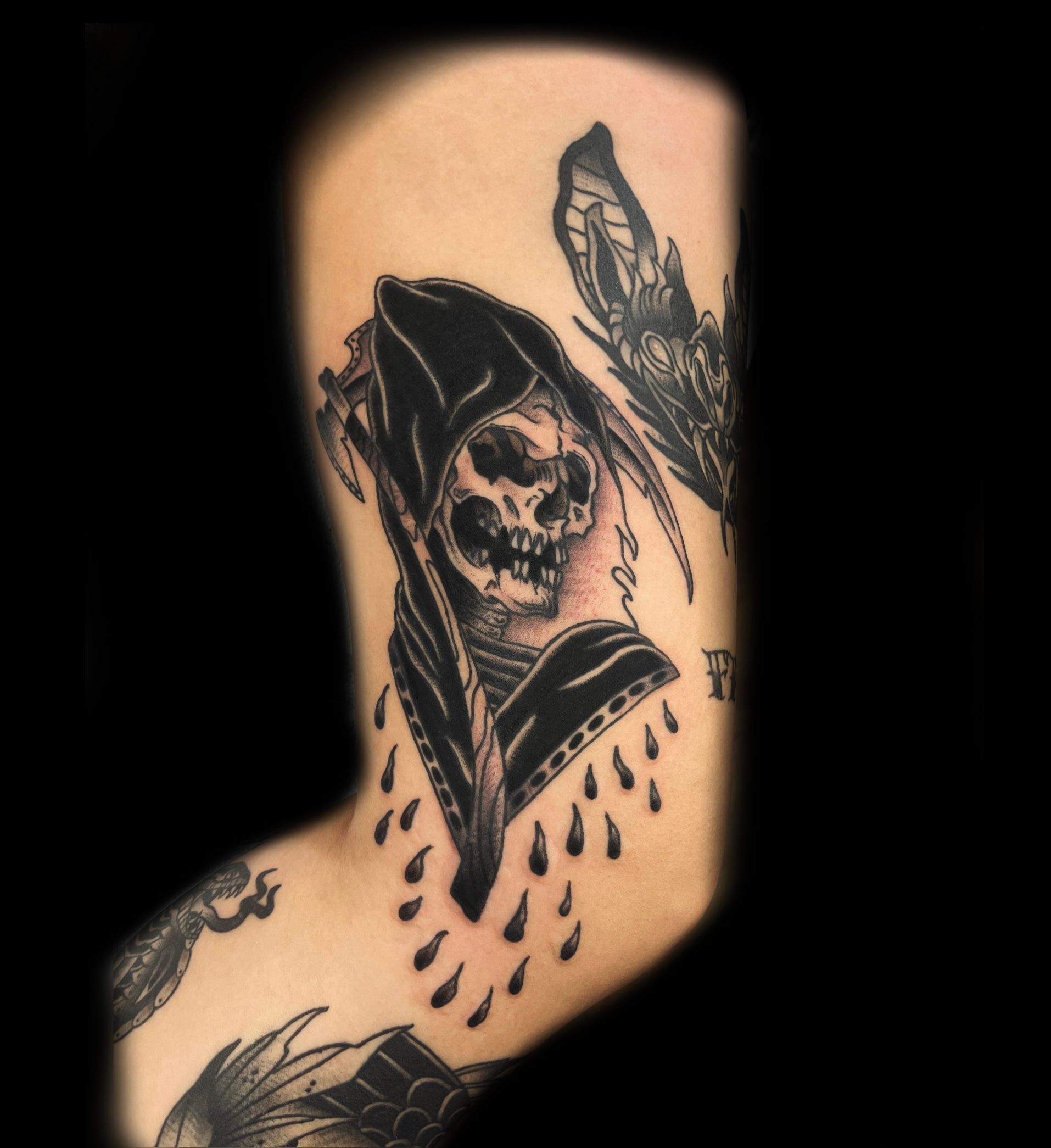 Tattoo of a skull in a hooded cloak, with dripping teardrops and a butterfly on an arm.