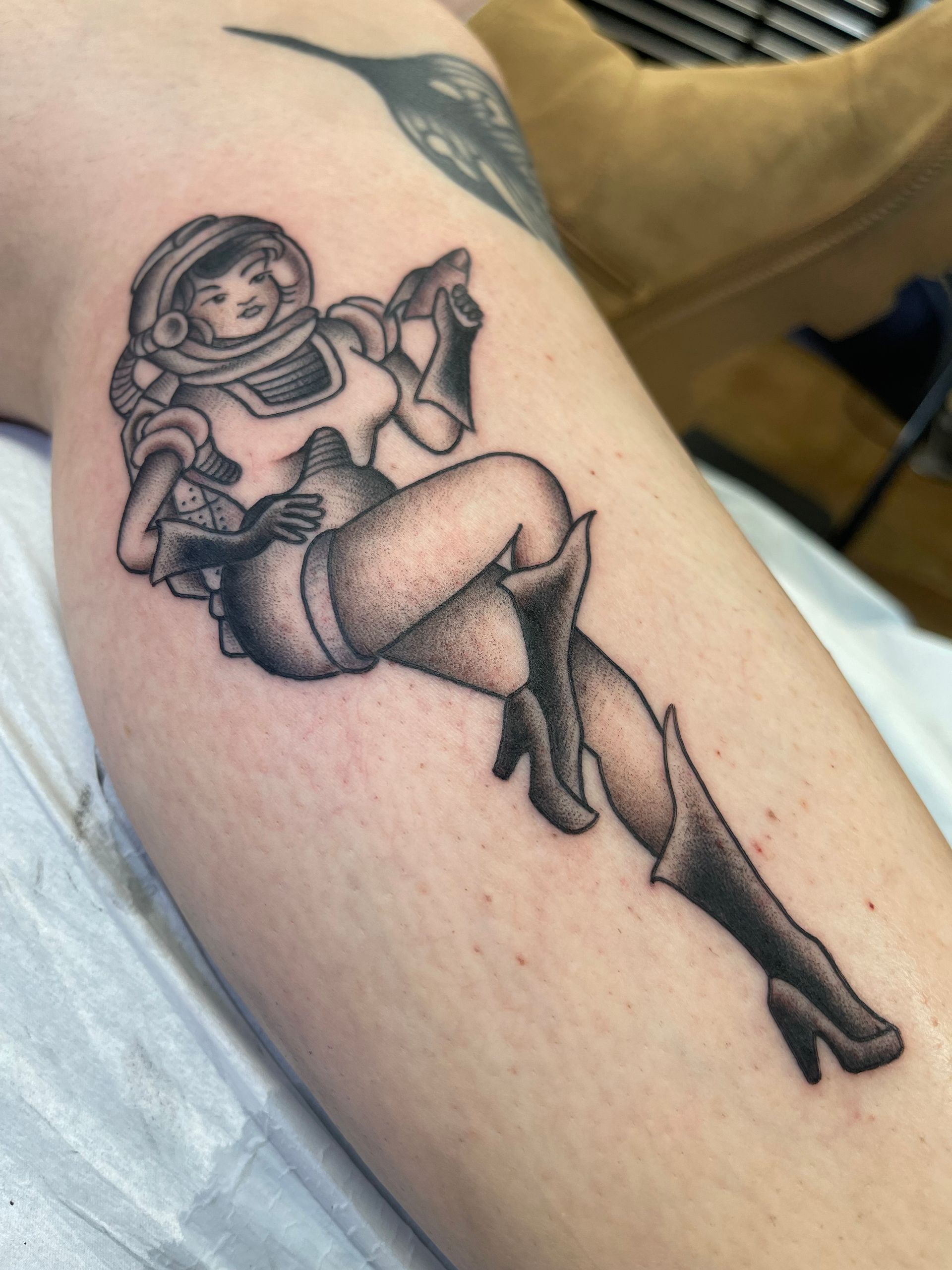 Tattoo of a woman in an astronaut suit, pin-up style, with dot shading.