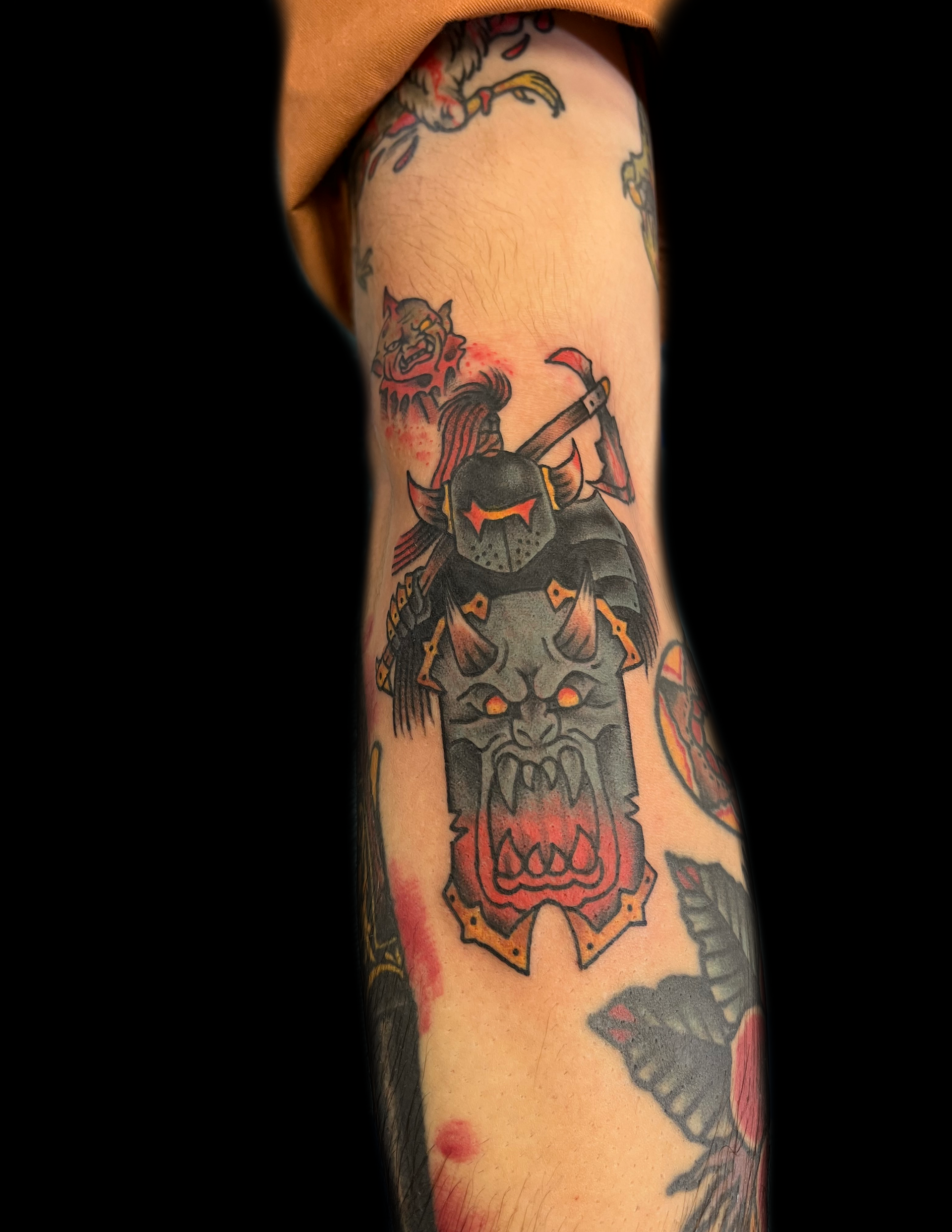 Arm tattoo of a monster with an axe, grey and red colors.