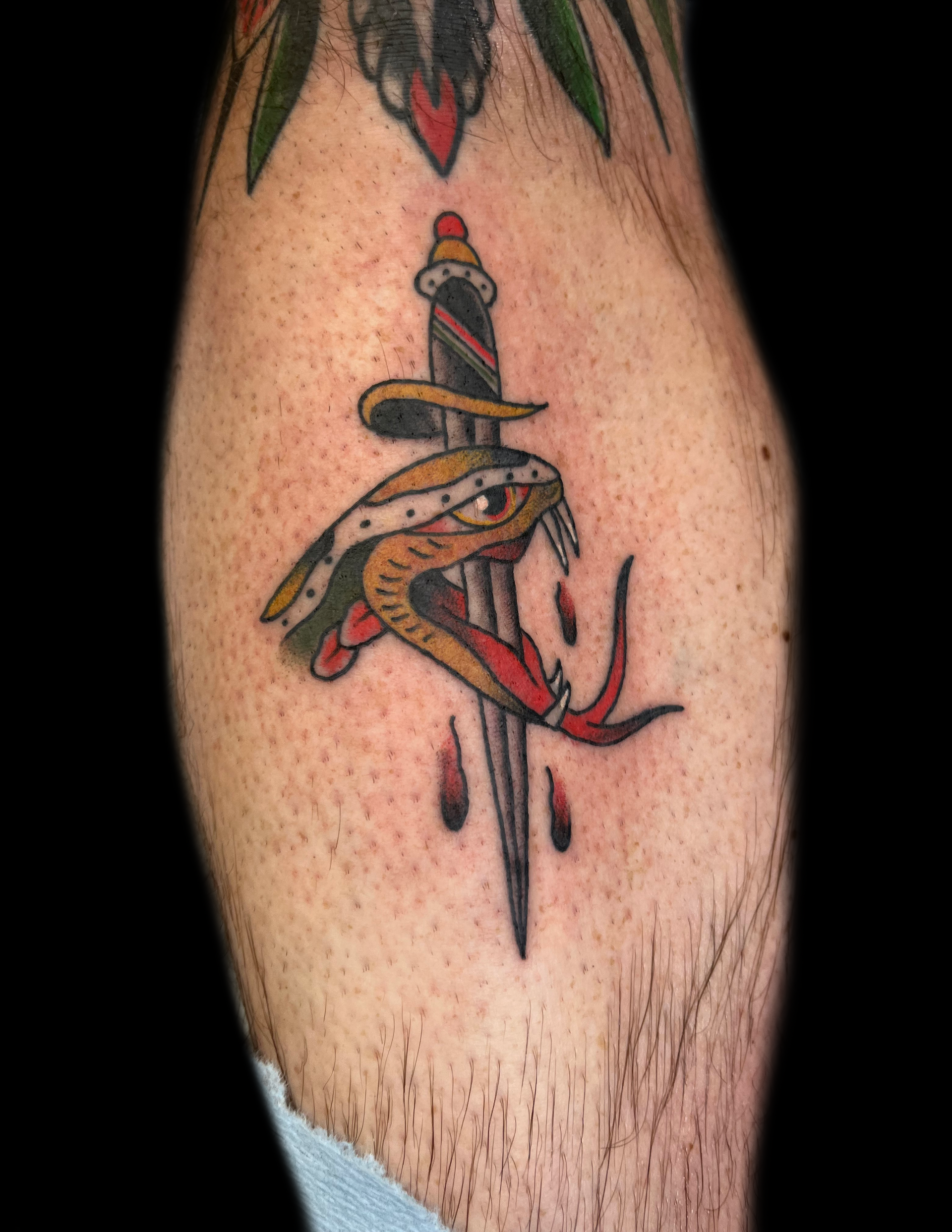 Tattoo of a snake with its mouth open, pierced by a dagger, with three blood drops.