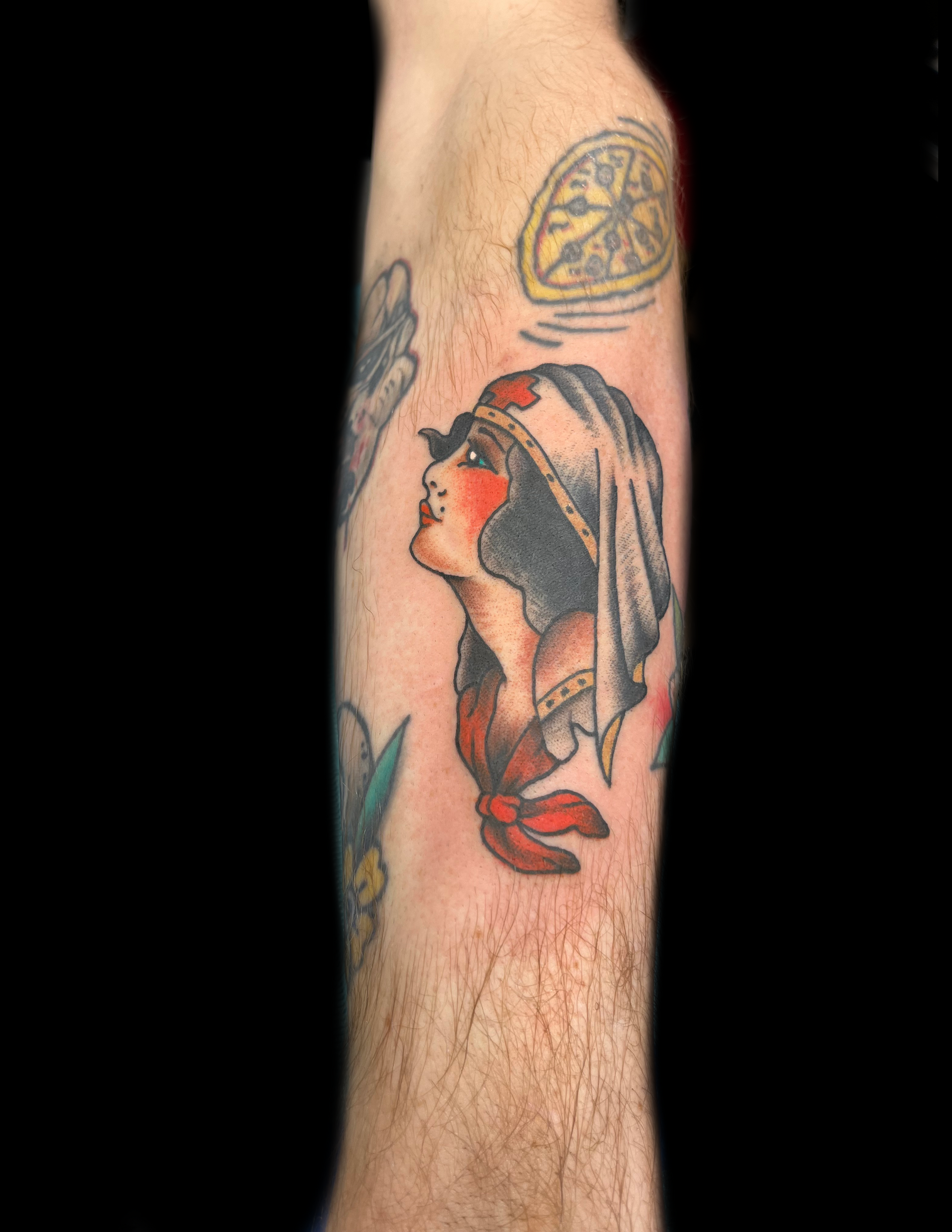 Tattoo of a woman looking upward, wearing a head covering. Red and black ink on arm.
