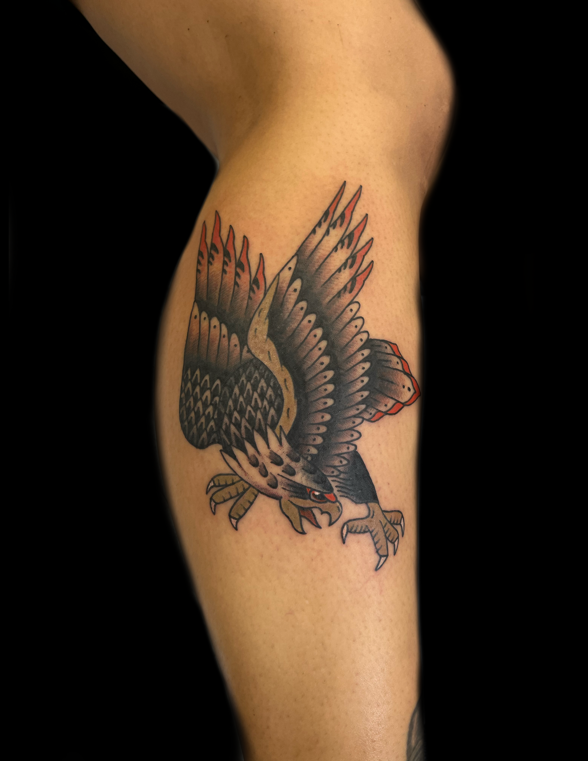 Tattoo of a black, white, and red eagle with outstretched wings on a leg.