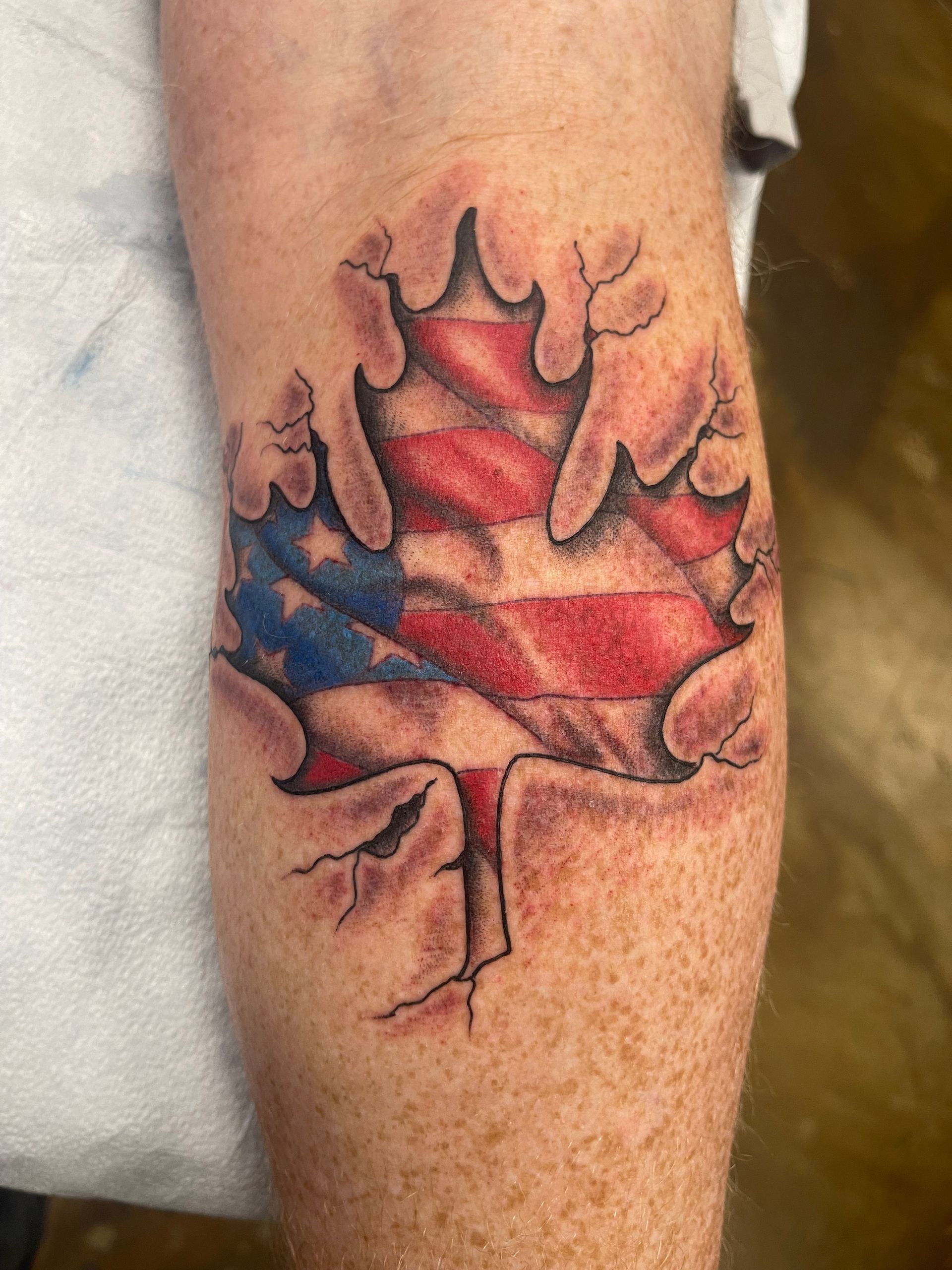 Tattoo on leg: Maple leaf with torn edges revealing an American flag.