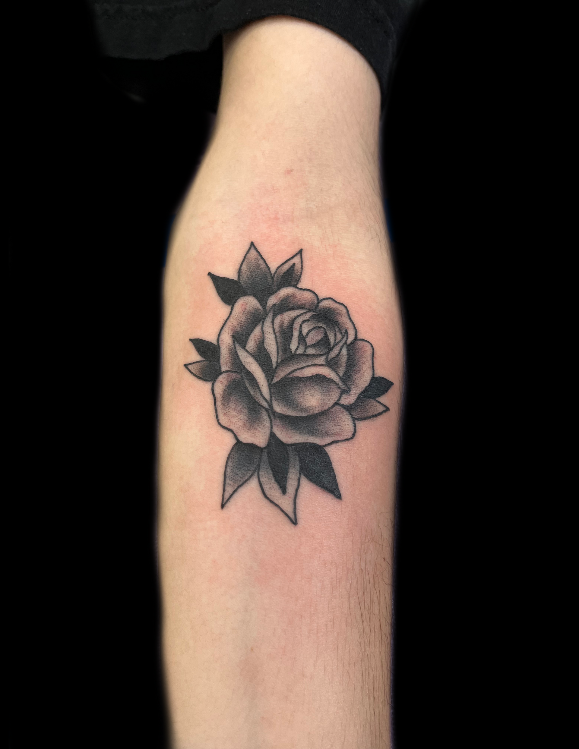 Black and gray rose tattoo on a person's forearm against a black background.