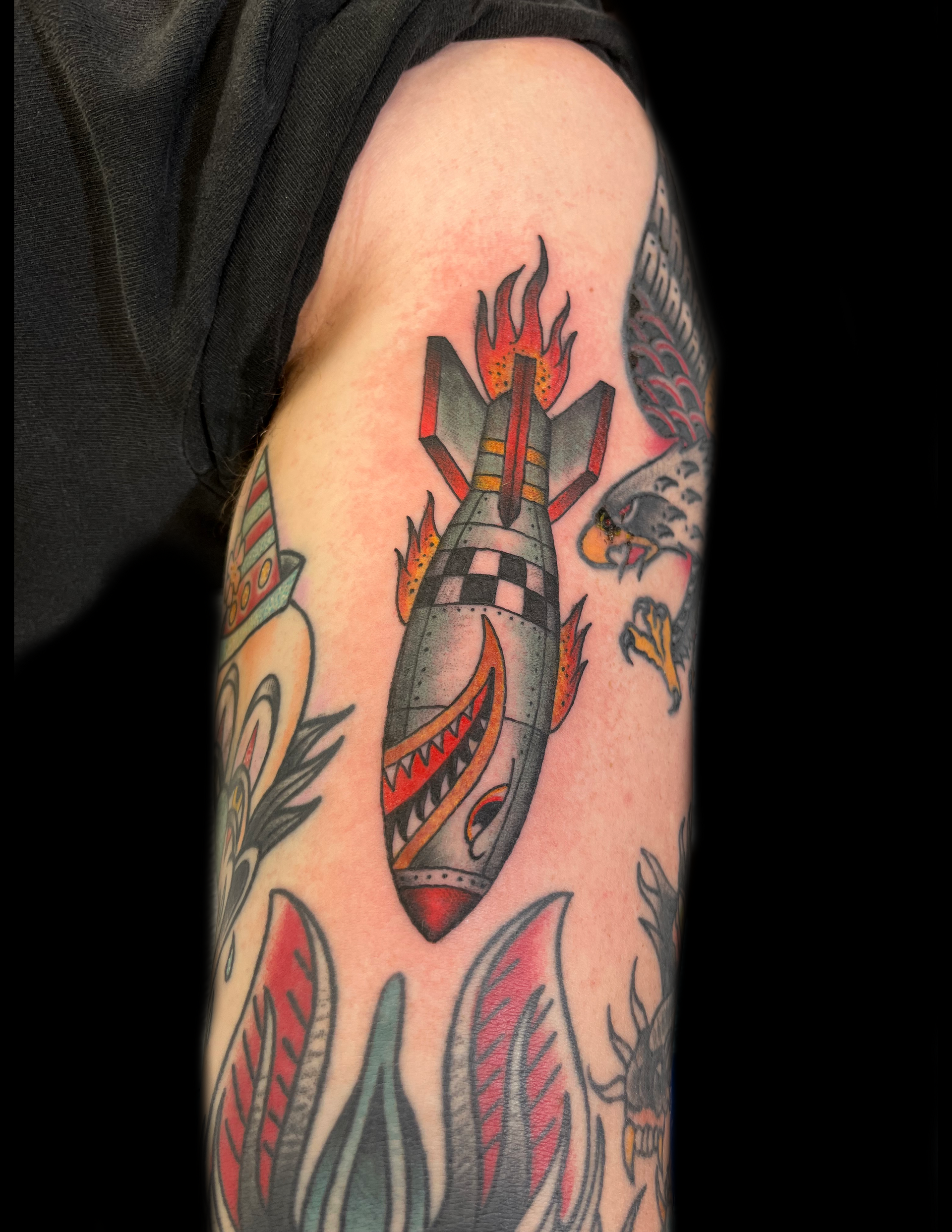 Tattoo of a bomb with a shark mouth and flames on arm, surrounded by other tattoos.