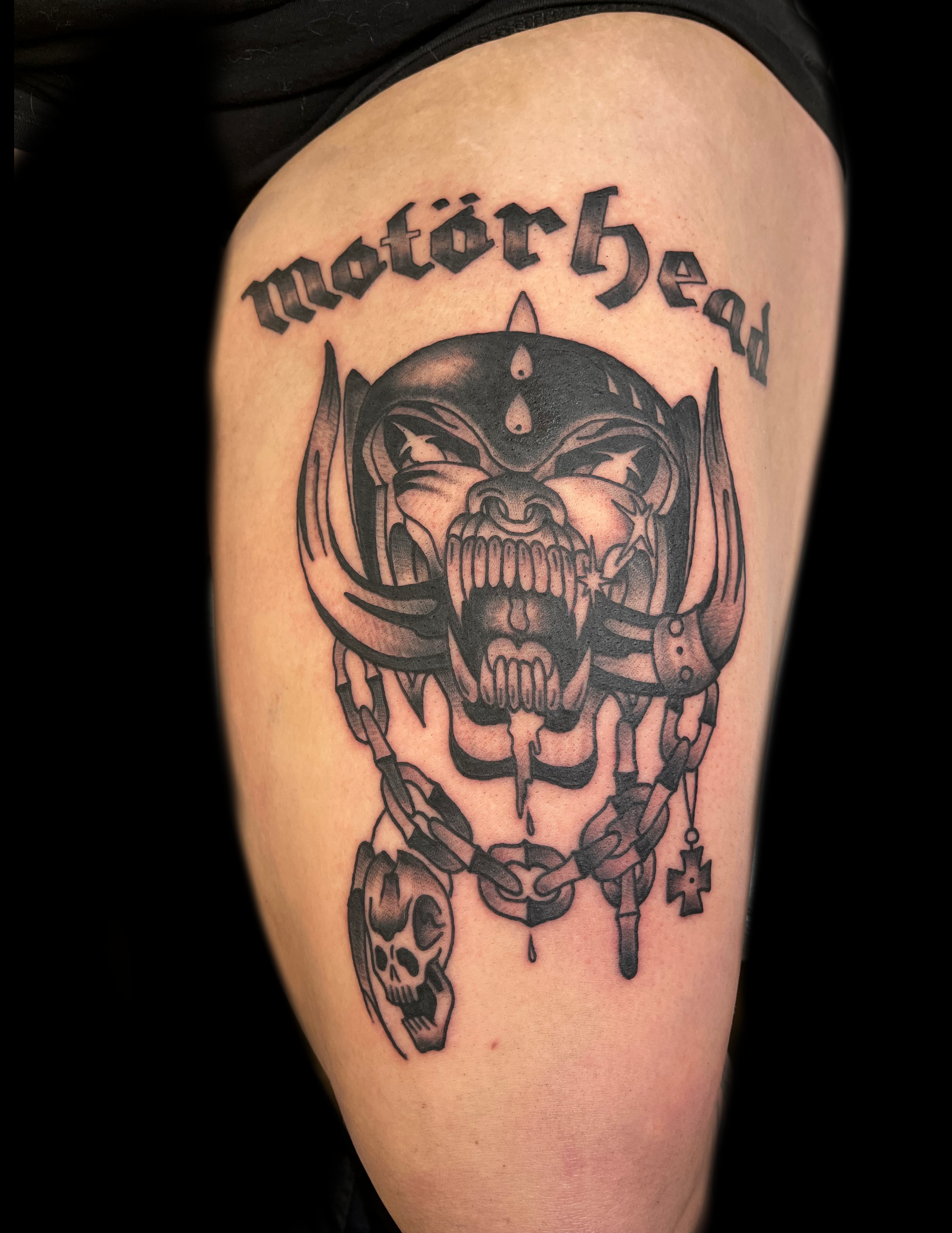 Motörhead tattoo of snarling skull with tusks and chain accessories on thigh.