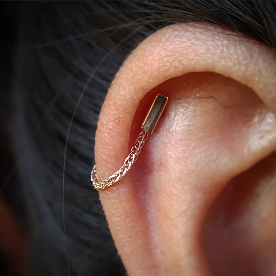 Close-up of an ear with a gold chain earring and dark hair