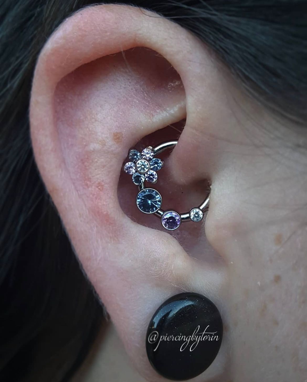 Close-up of an ear wearing a jeweled curved ear cuff and a black gauge plug